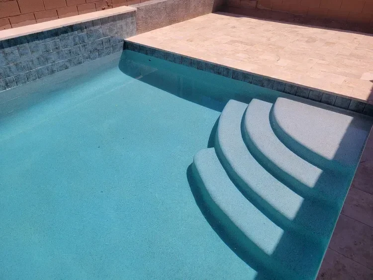 Swimming pool with blue water, rounded steps, tiled walls, and a surrounding stone patio.
