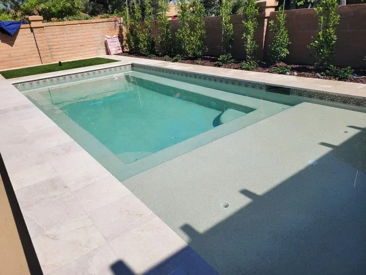 Backyard swimming pool with tiled edge and surrounding greenery, enclosed by a brick wall.