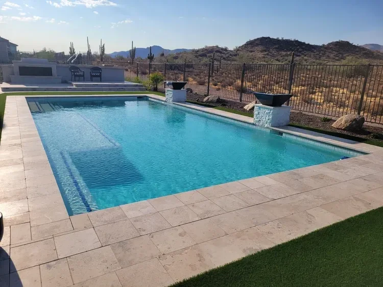 Swimming pool with tile deck, desert landscape, mountains, and cacti in the background.