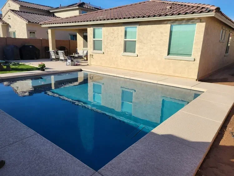 Residential backyard with a swimming pool and patio area, featuring outdoor furniture and a beige stucco house.