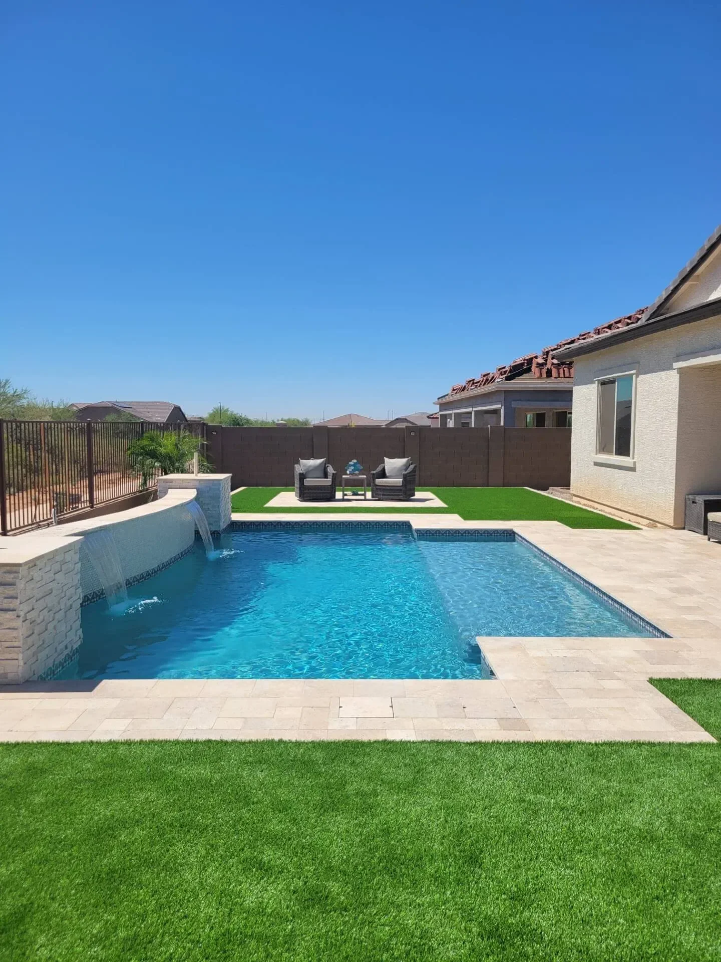 Backyard with swimming pool, stone waterfall, artificial grass, and outdoor seating on a sunny day.