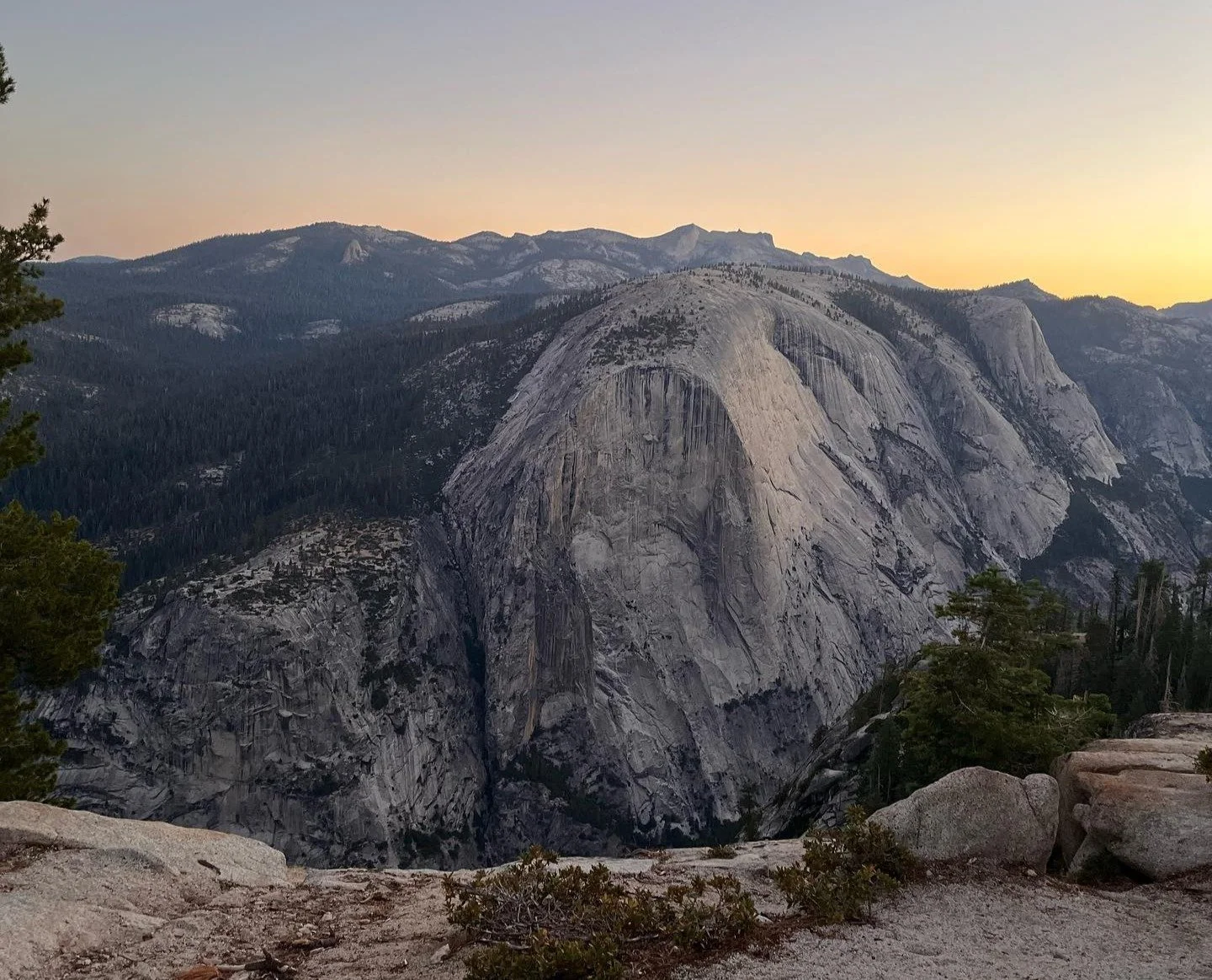 Scenic view of Half Dome granite formation in Yosemite National Park at sunset, with rocky foreground and mountains in background.