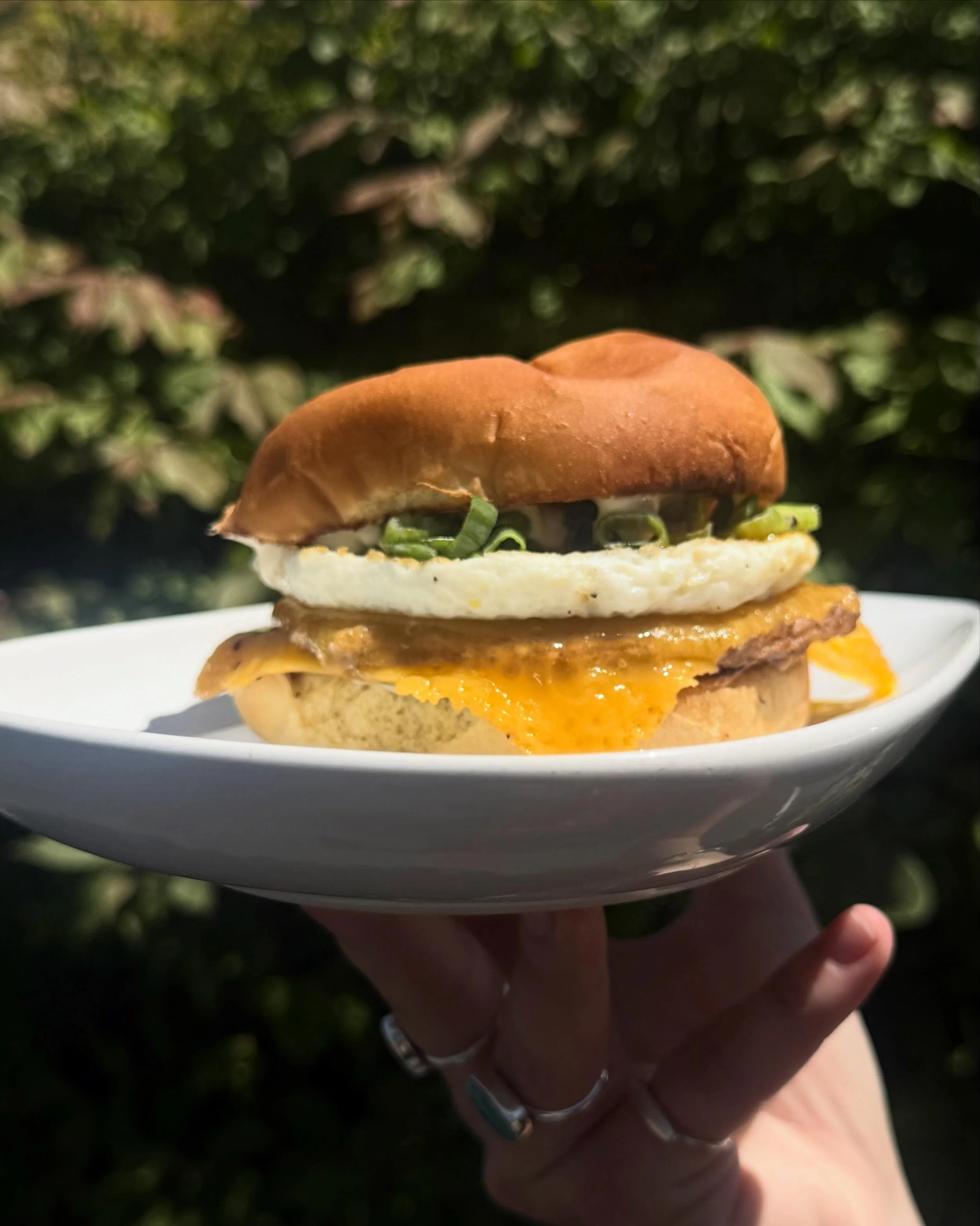 Can you help us pick which photo is the best to show off our new breakfast sandwich? Let us know tomorrow when you come in and try it for yourself! A sausage patty, cheddar cheese, an egg patty, green onions, hot honey, garlic aioli, all on a toasted