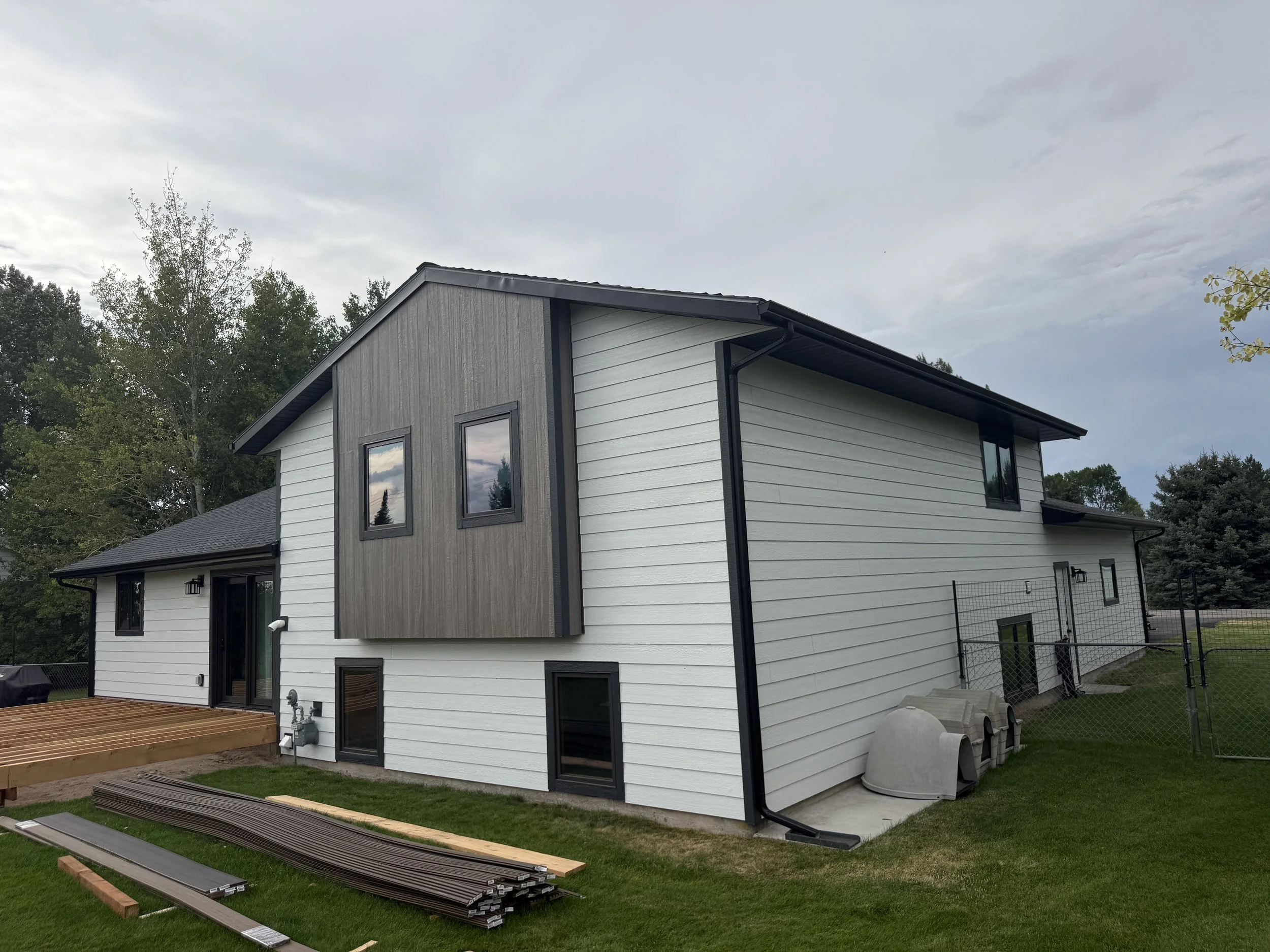 New two-story house with white siding and black window frames, gray accents, and a wooden deck under construction in the backyard.