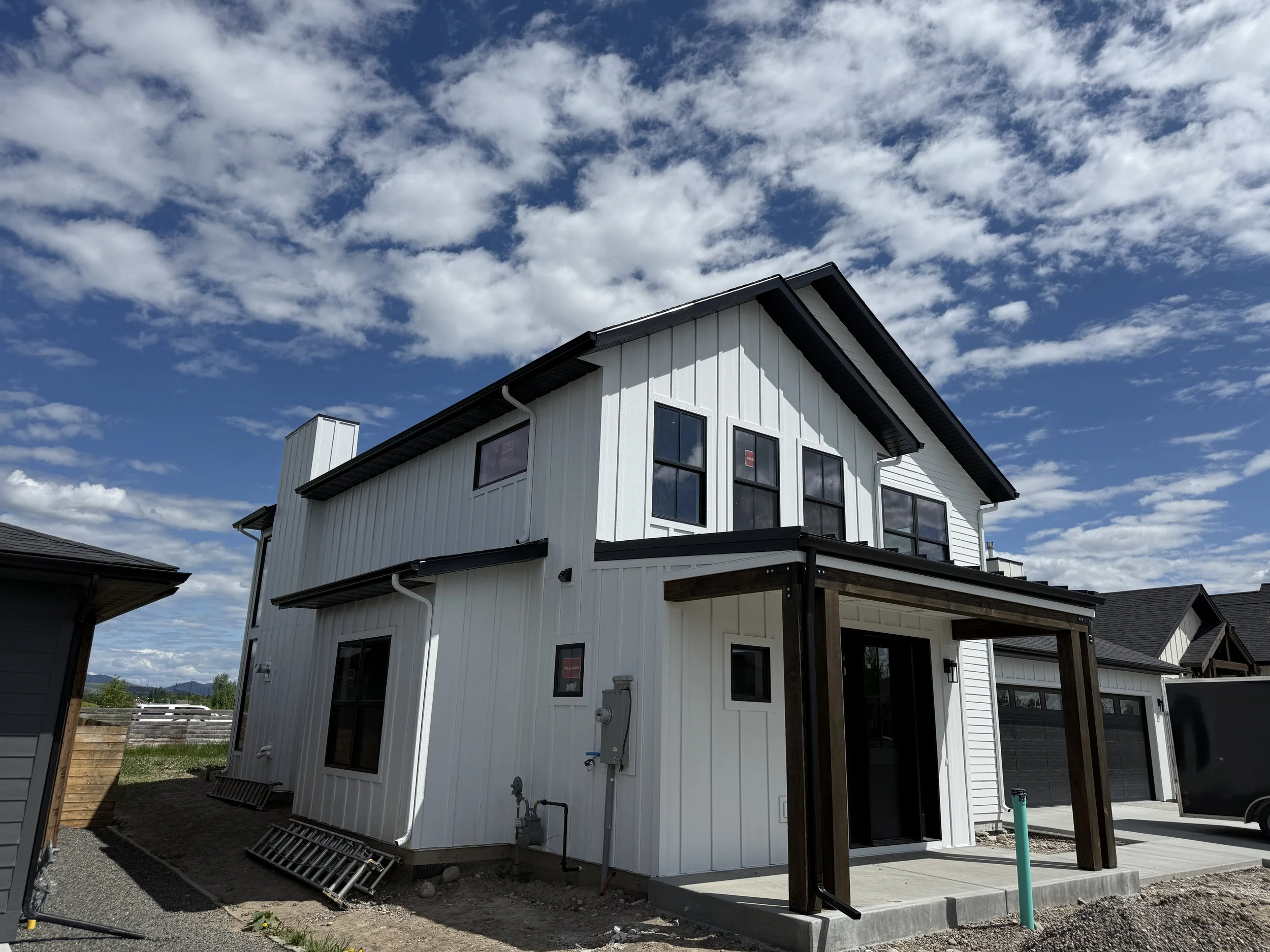 New two-story white house under a partly cloudy sky, featuring black window frames, a black roof, and a small covered porch.