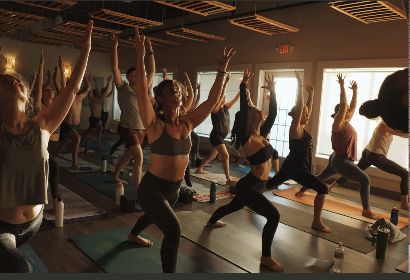 Group of people participating in a yoga class with sunlight coming through windows.