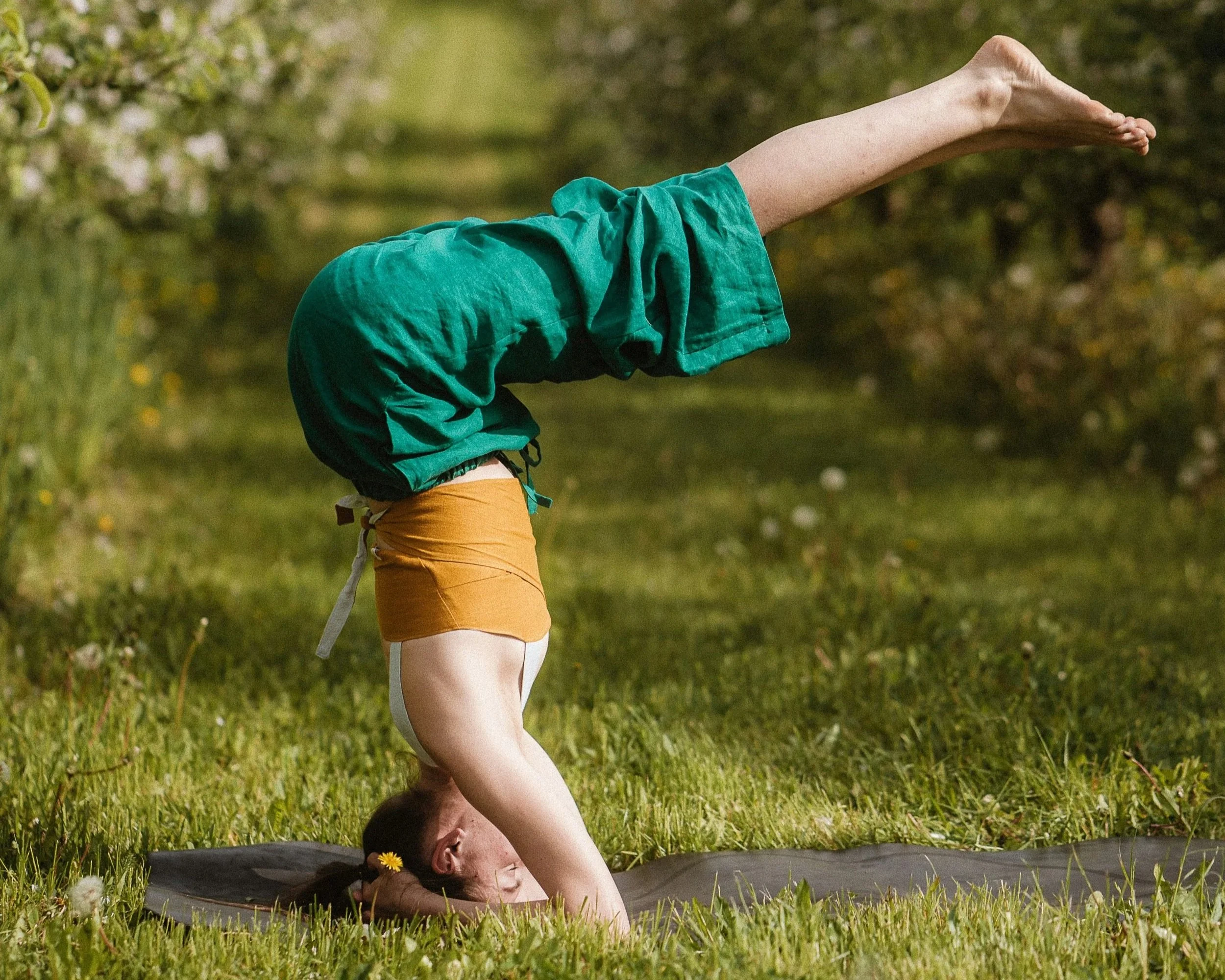 A woman practicing yoga outdoors on a grassy field, performing a headstand pose.