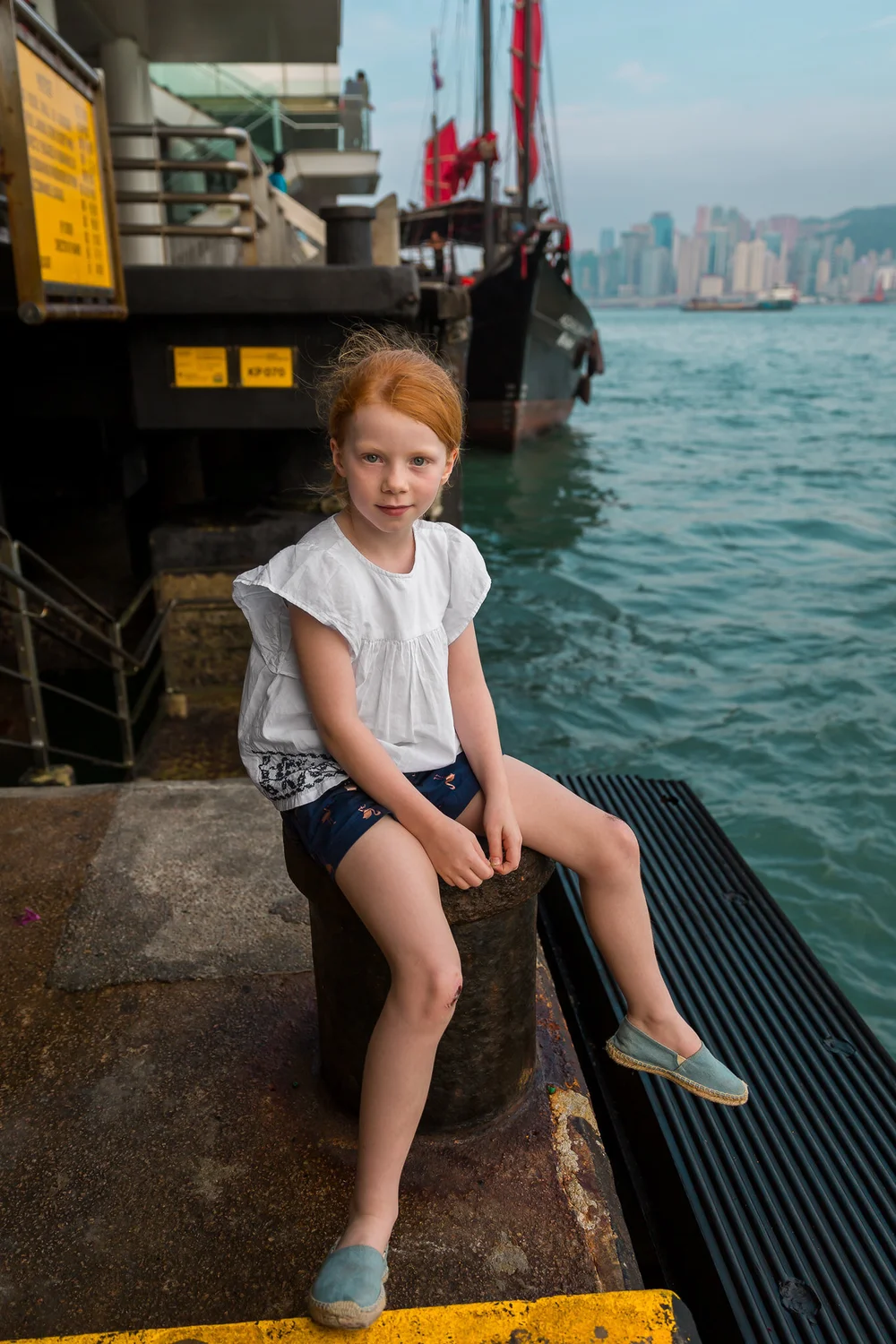 A girl with red hair sits on the edge of Victoria Harbour, TST