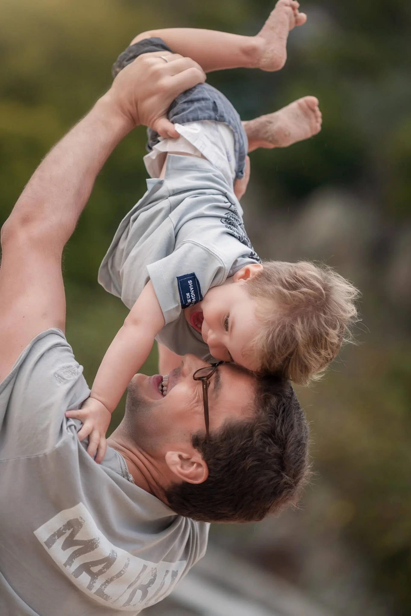 A man playfully holding a laughing kid upside down outdoors.