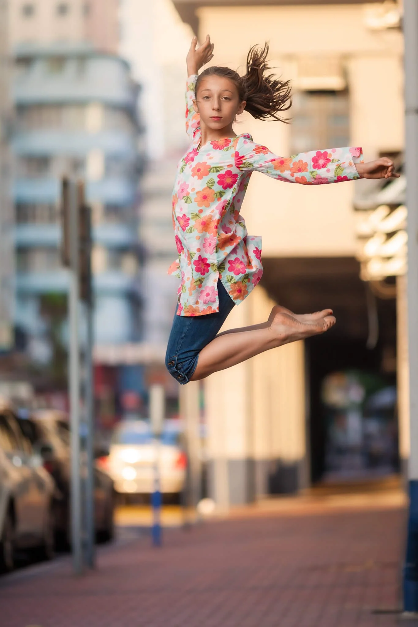 Girl in a floral dress jumping mid-air on a city street.