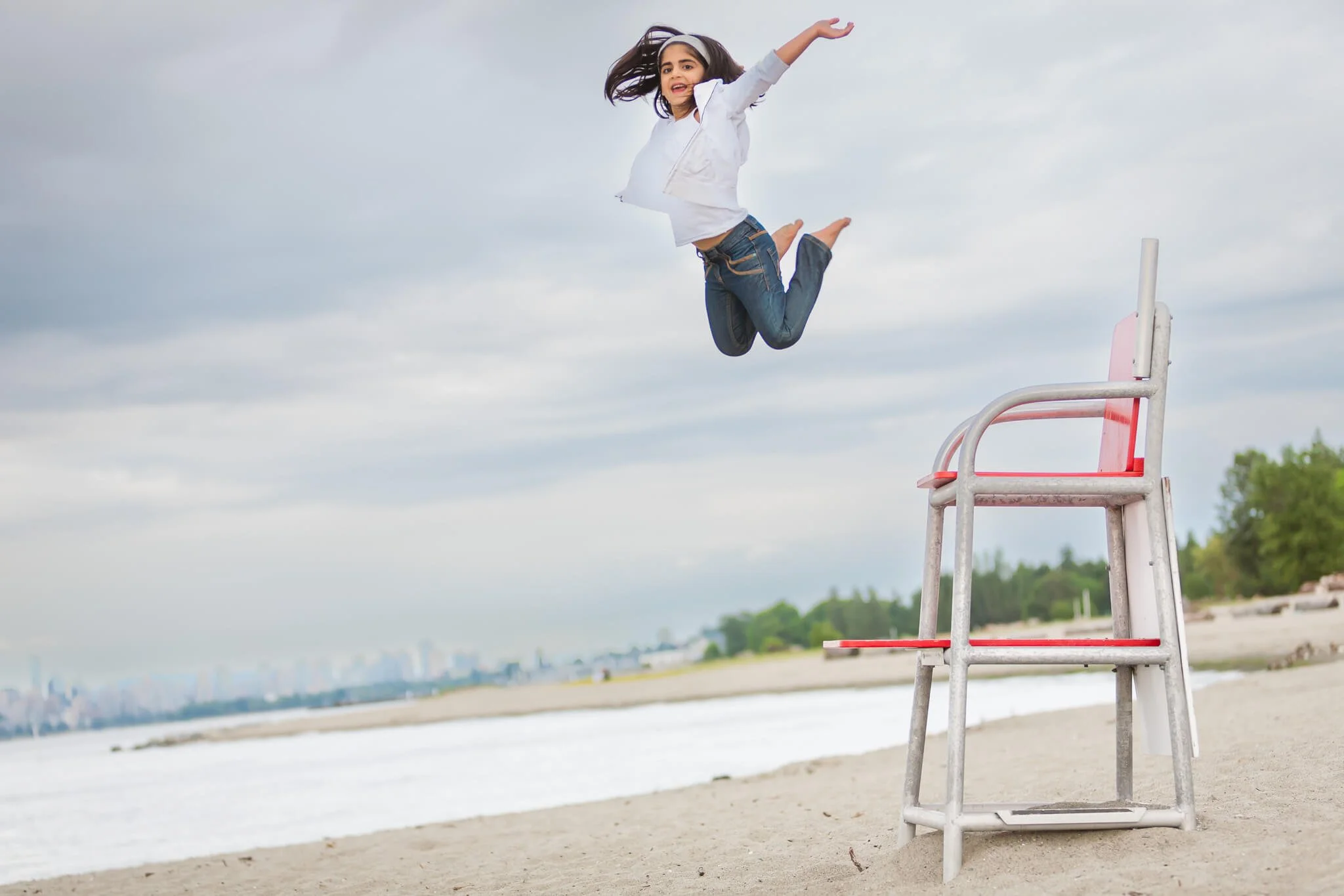 In Vancouver an athletic girl jumps off a lifeguard stand on Kitsilano Beach