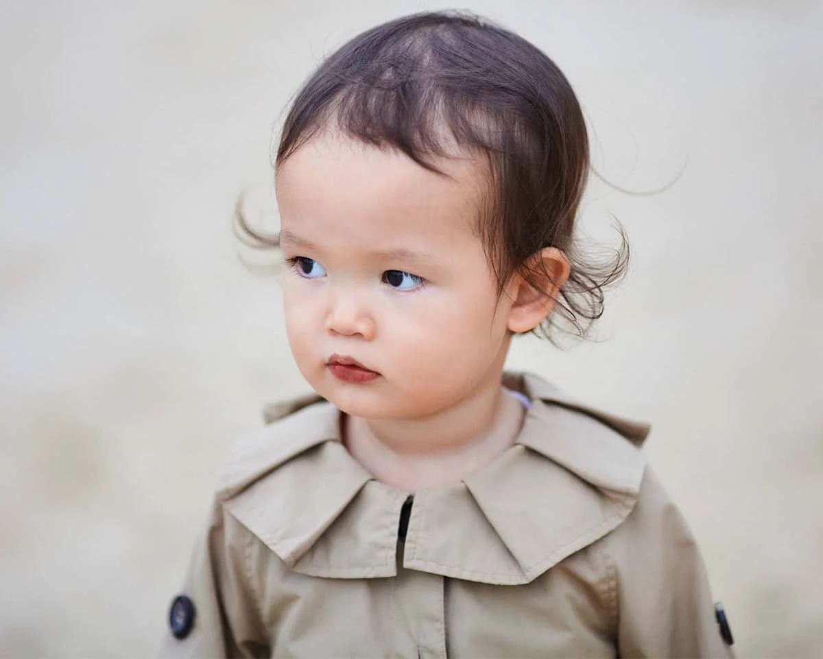 Young child wearing a tan coat with a serious expression.