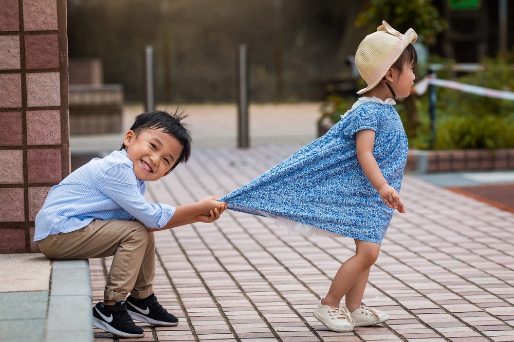 Kid playfully tugs at his sister's dress in Kowloon on a family photoshoot in Hong Kong