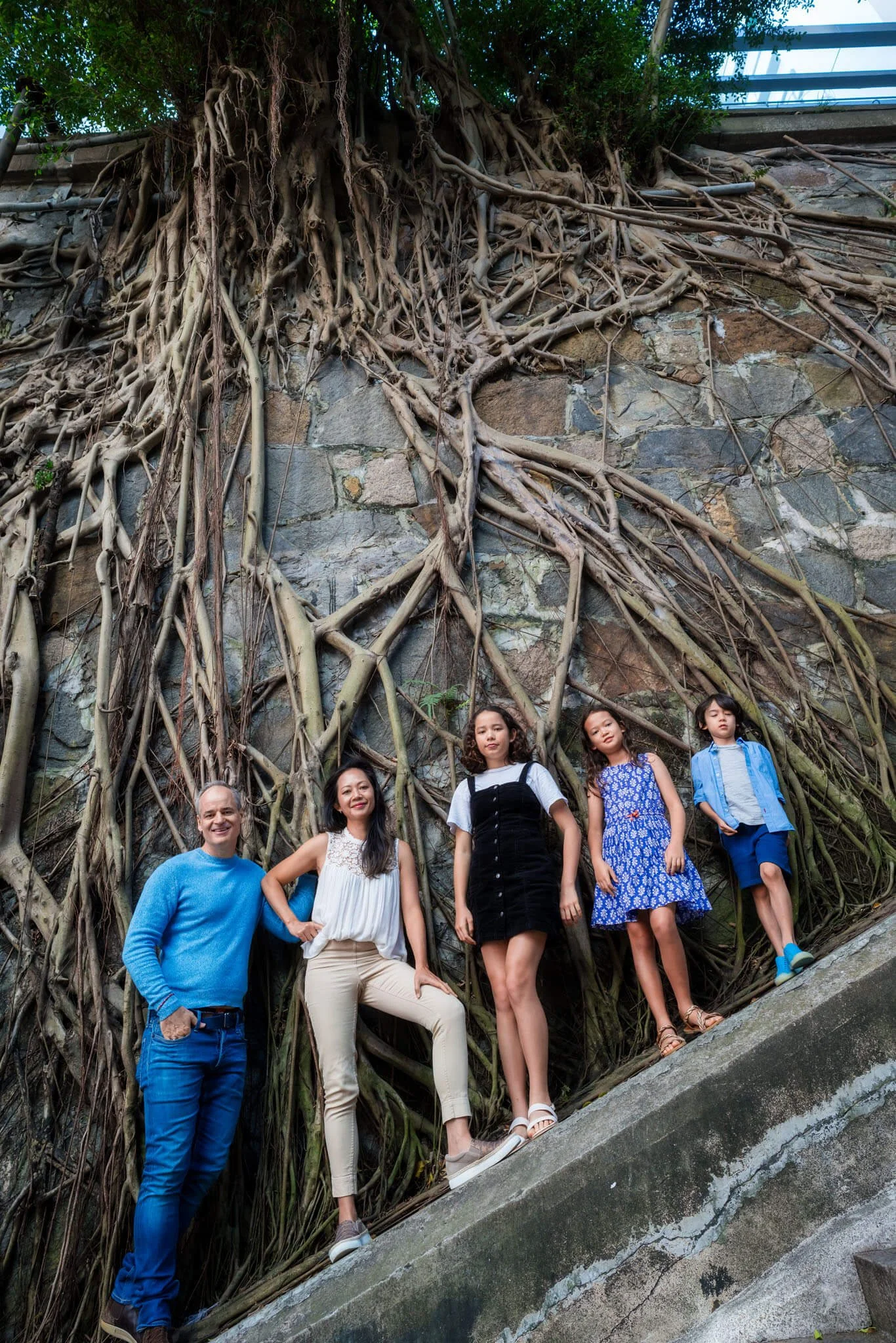 Family of five pose in front of a wall and huge trees roots on Hollywood Road HK