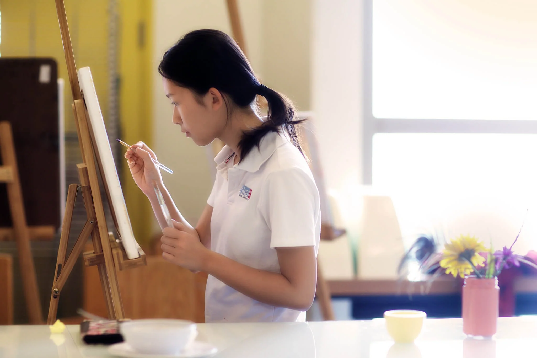 At Hong Kong Academy a girl works on a watercolour painting in a well lit room.