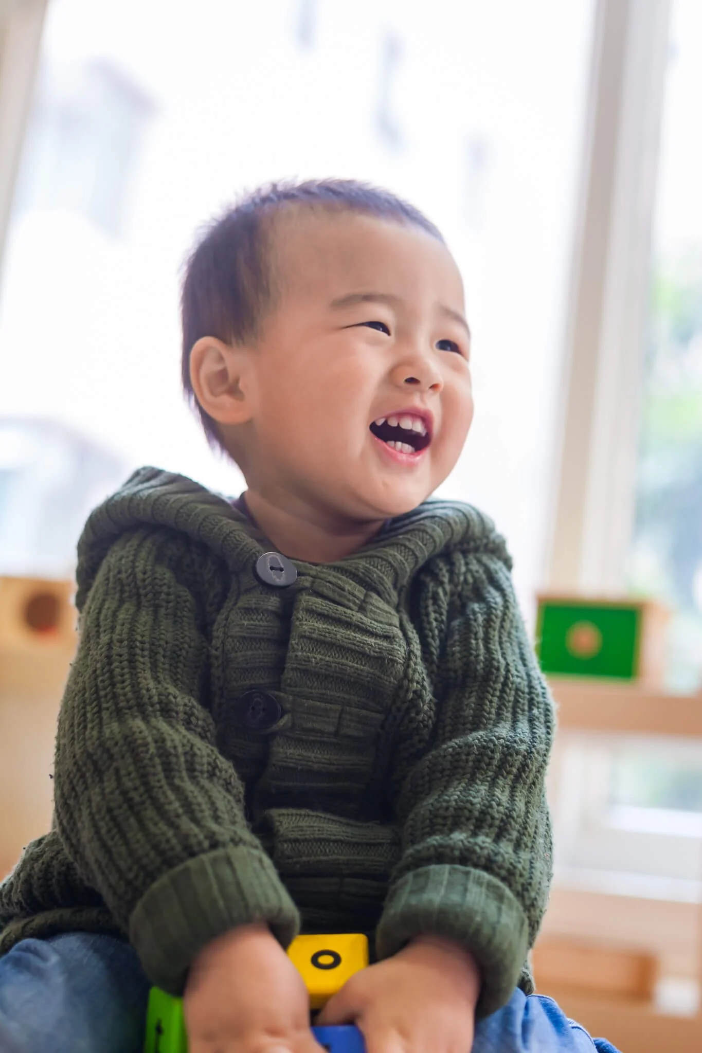 A smiling child in a green knitted sweater indoors at a school photo shoot in Hong Kong