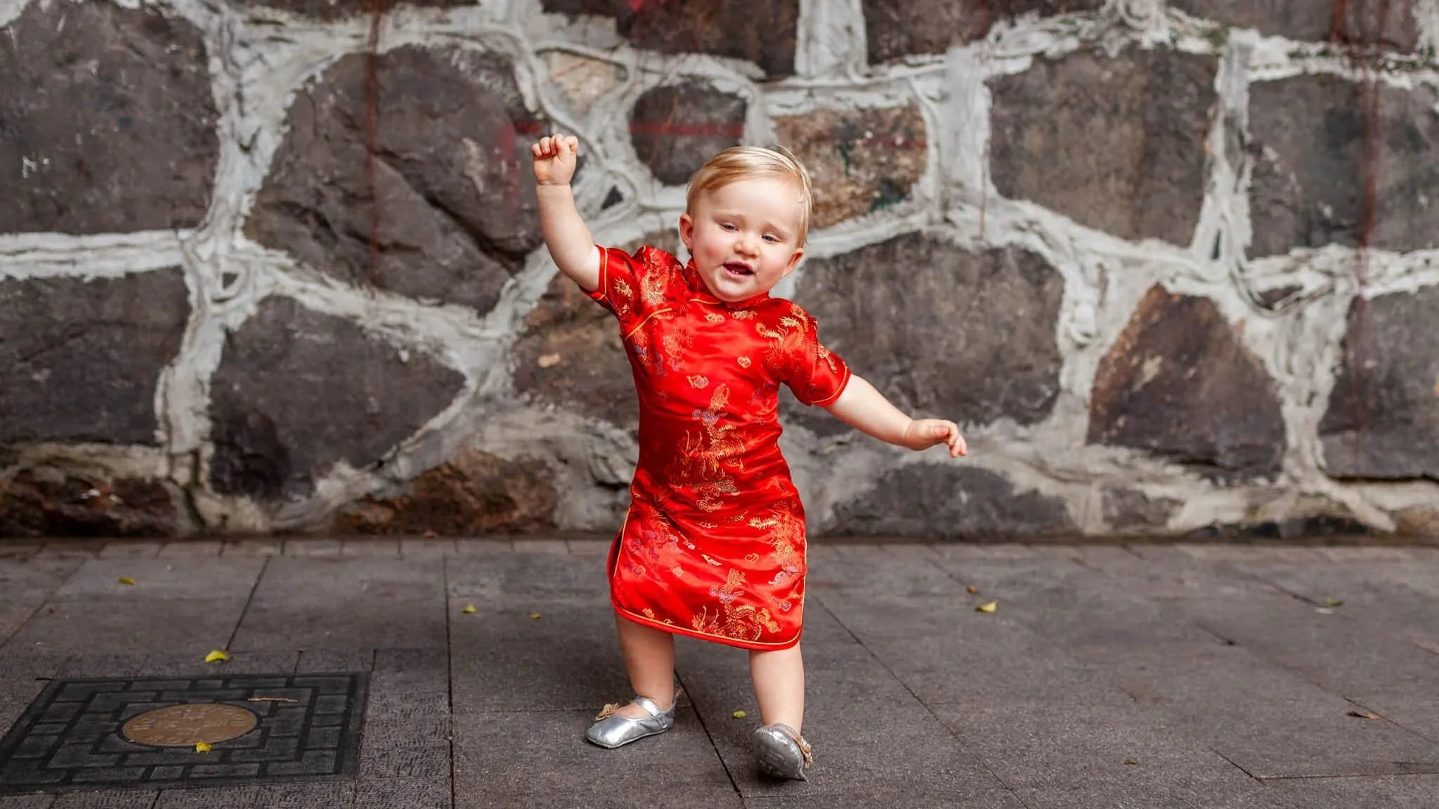Kid-led family photography in Hong Kong featuring a toddler dancing in a red cheongsam.