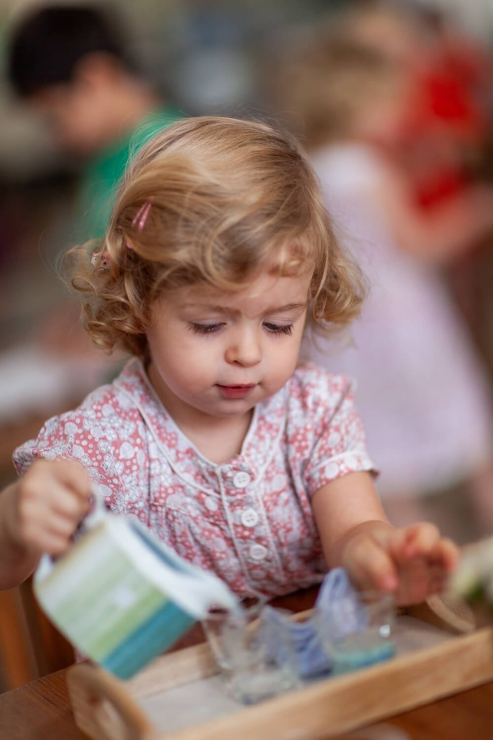 Girl carefully practicing a Montessori pouring activity, captured by professional school photographer Ian Taylor.