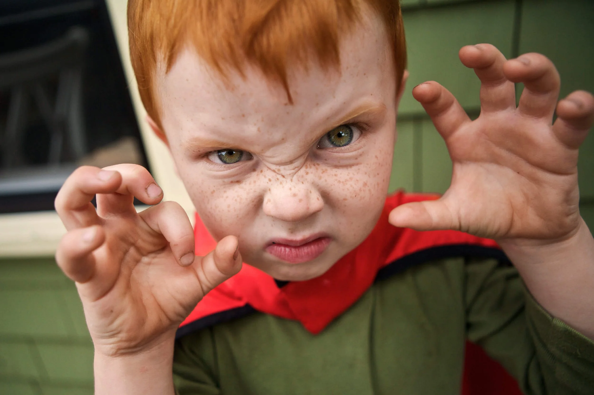 A red-haired boy in a superhero outfit makes a scary monster face.