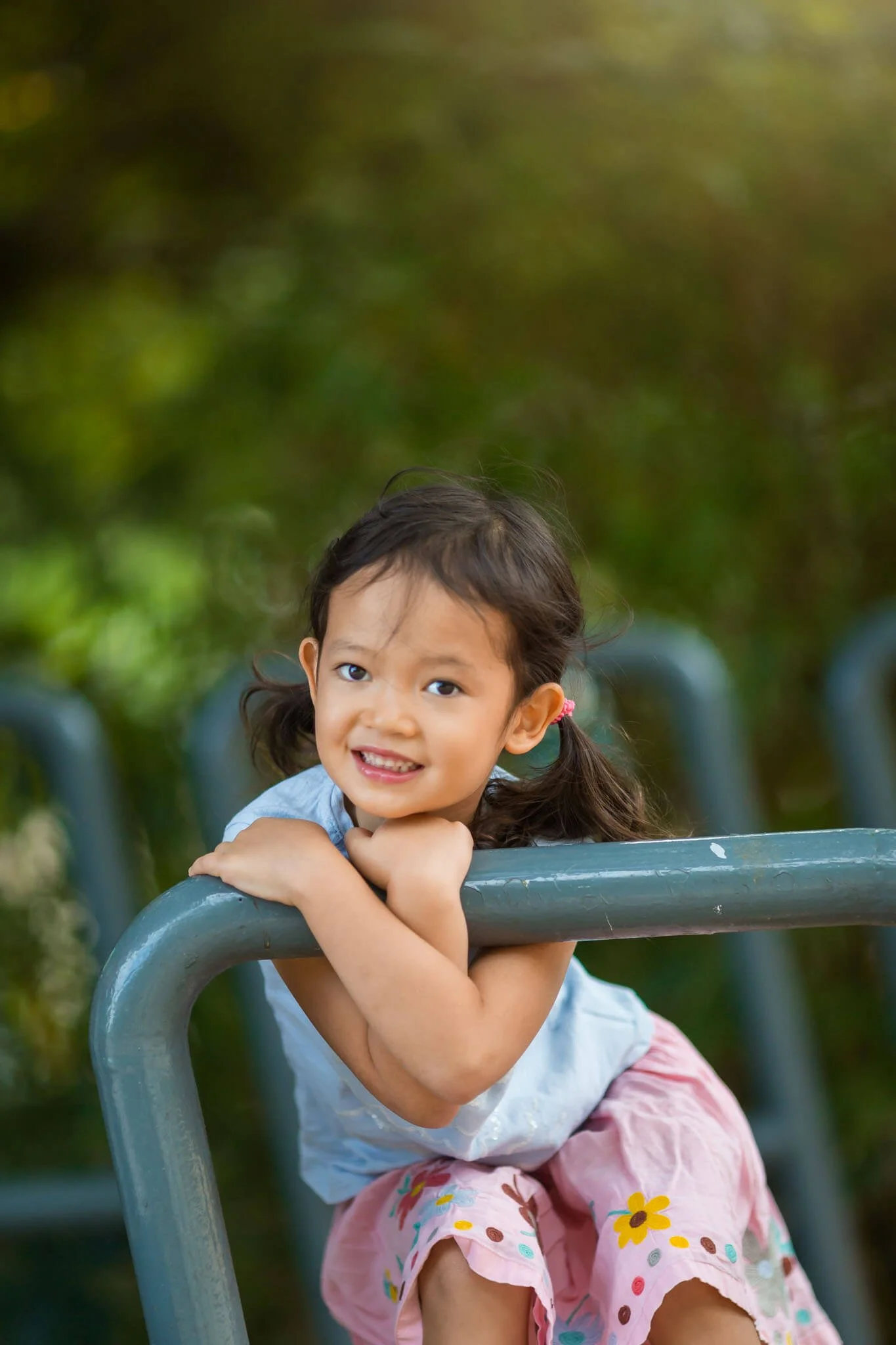 Young girl with pigtails hanging on a playground bar, smiling outdoors.
