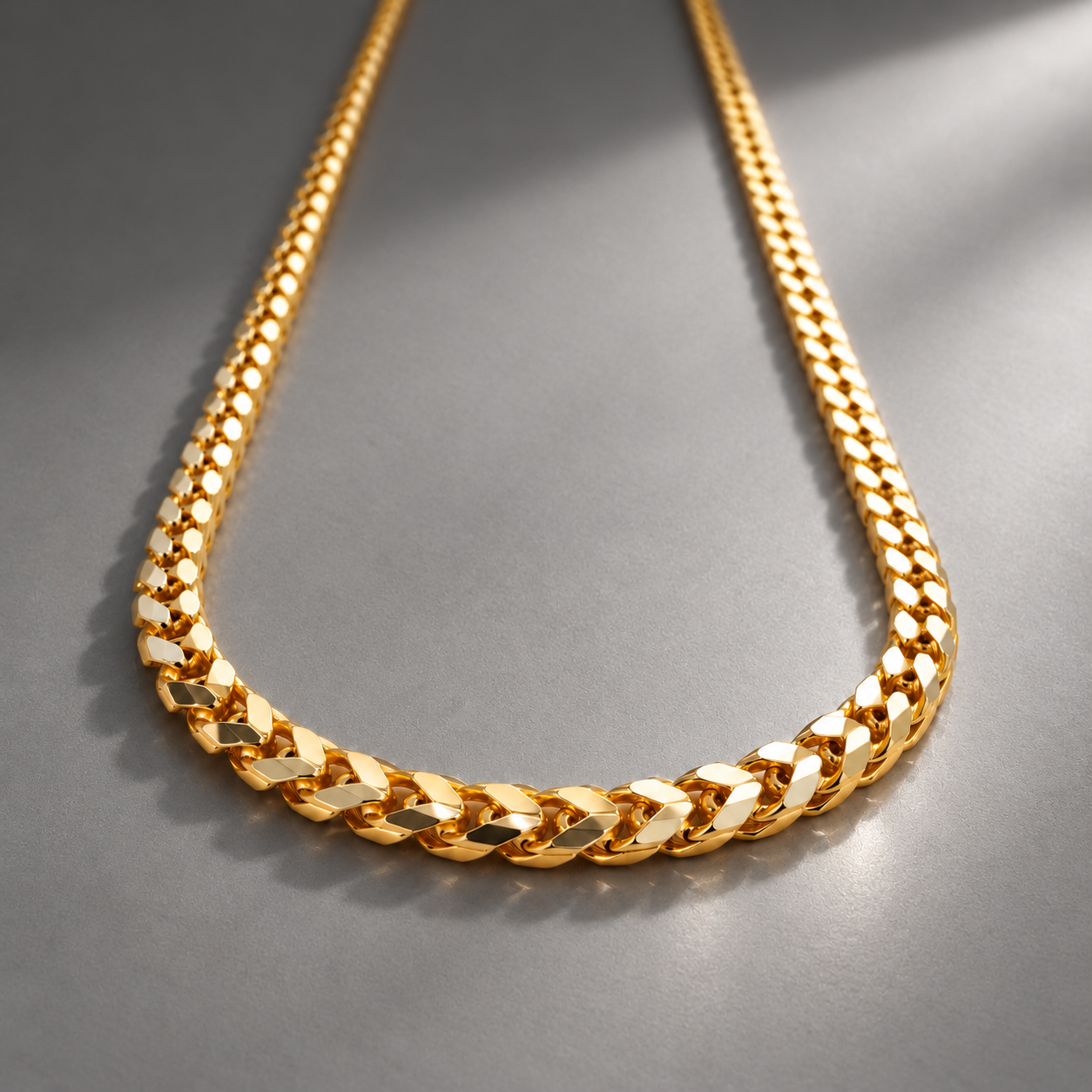 Gold chain necklace with a thick, linked design on a gray surface.