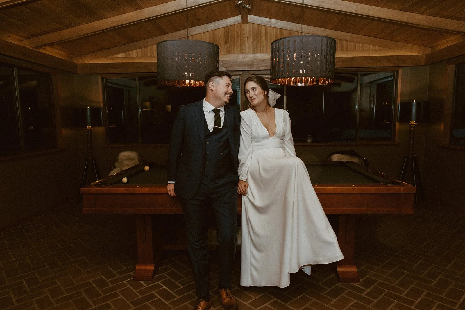 Bride and groom sit on a pool table inside their wedding venue in Washington State