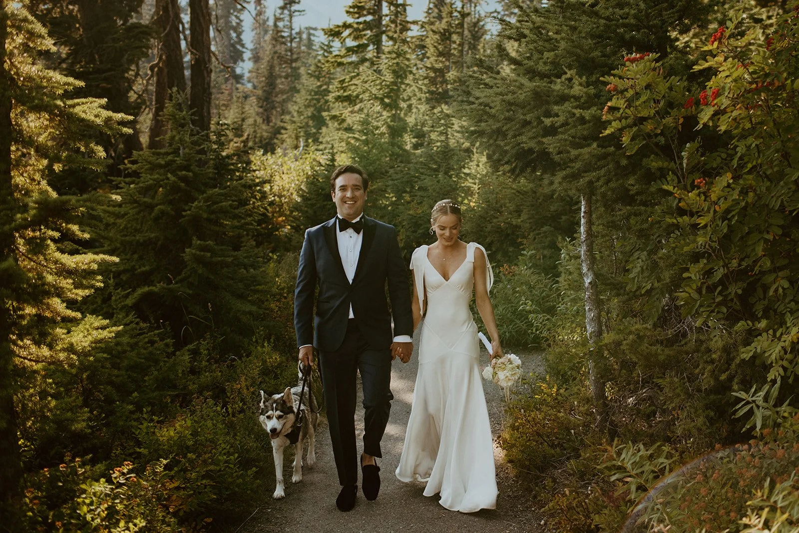 Bride and groom walk with their dog through a forested area of Artist Point