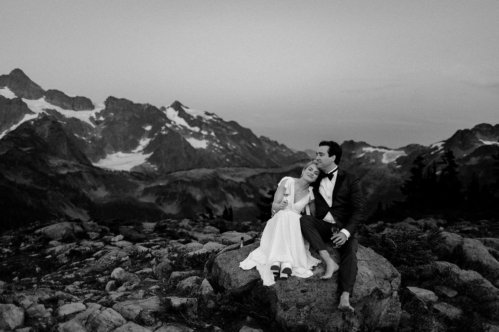 Bride and groom sit on a boulder at Artist Point sharing champagne at sunset