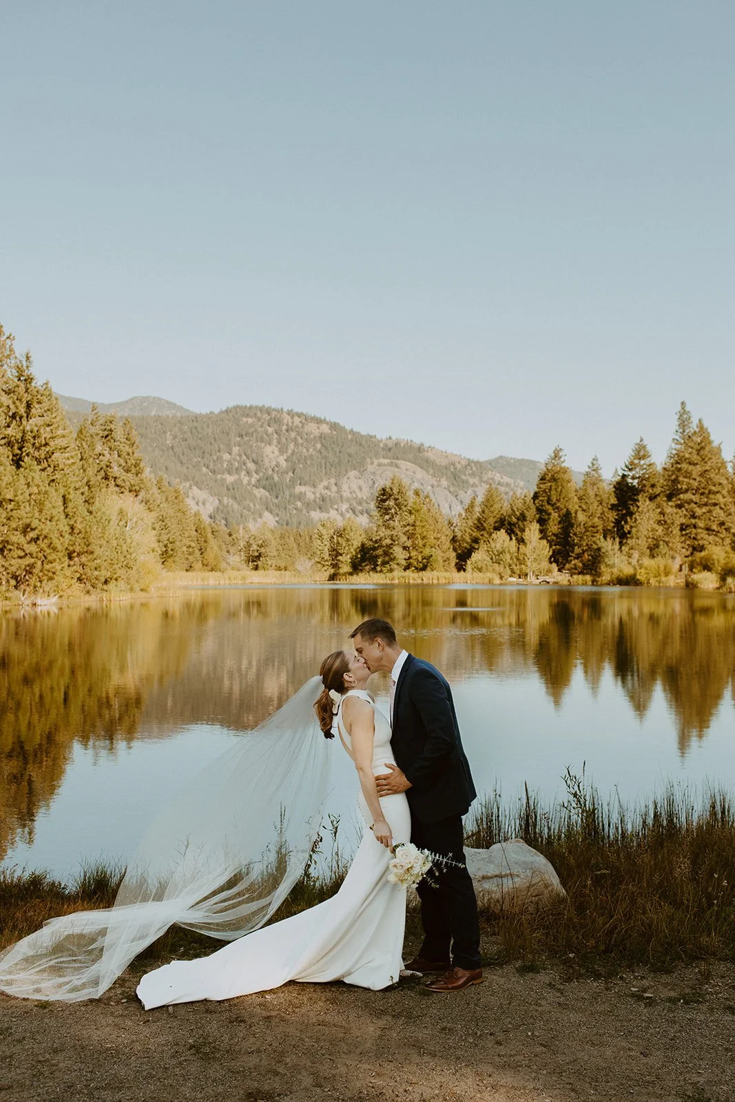 Bride and groom kiss next to a Washington mountain lake