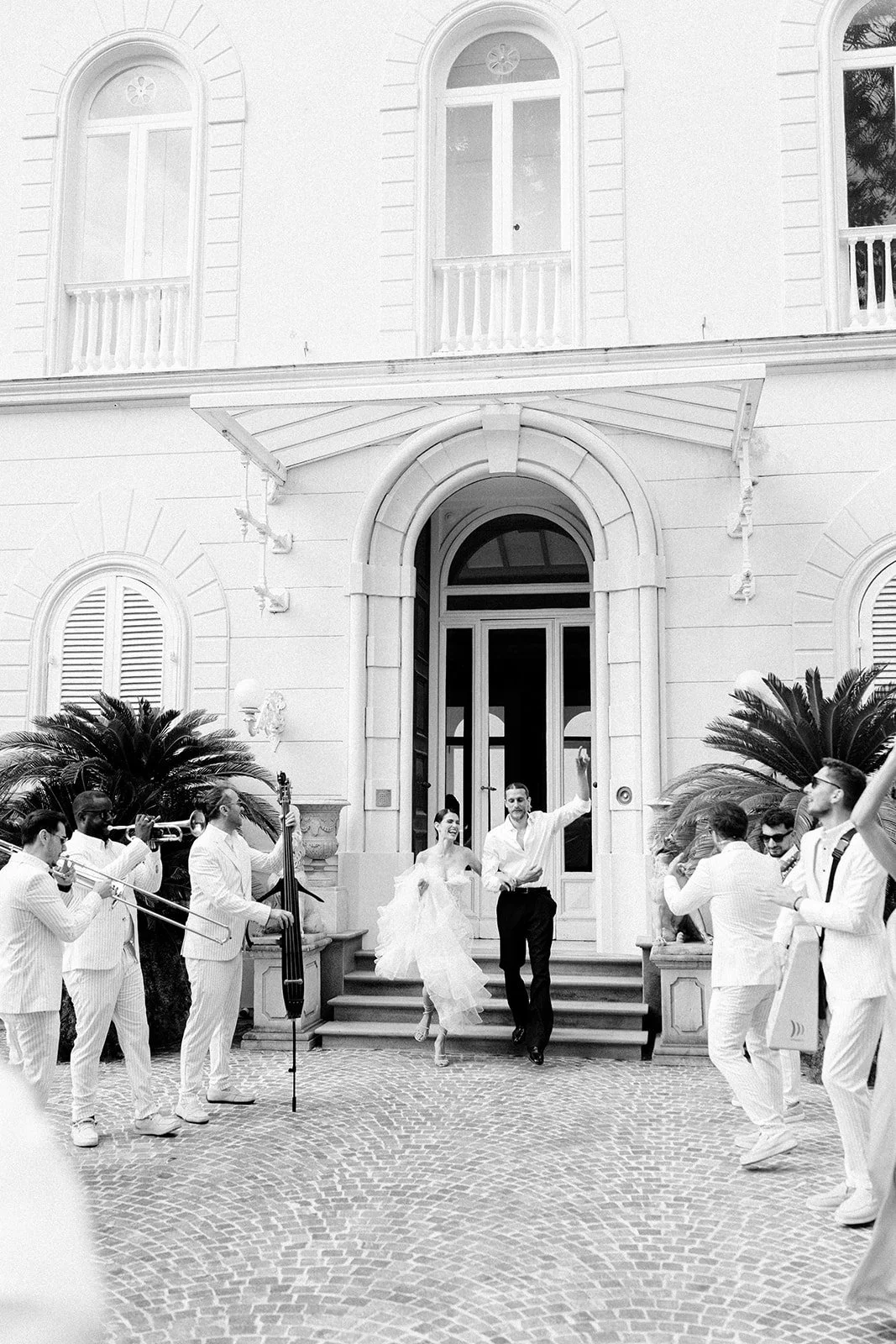 Bride and groom walk out of Villa Astor while a live band plays on both sides of them