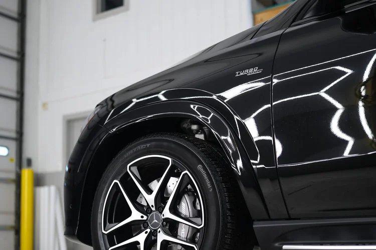 Black Mercedes AMG fender throwing an unbroken ceiling light reflection after paint correction at Ascension Automotive