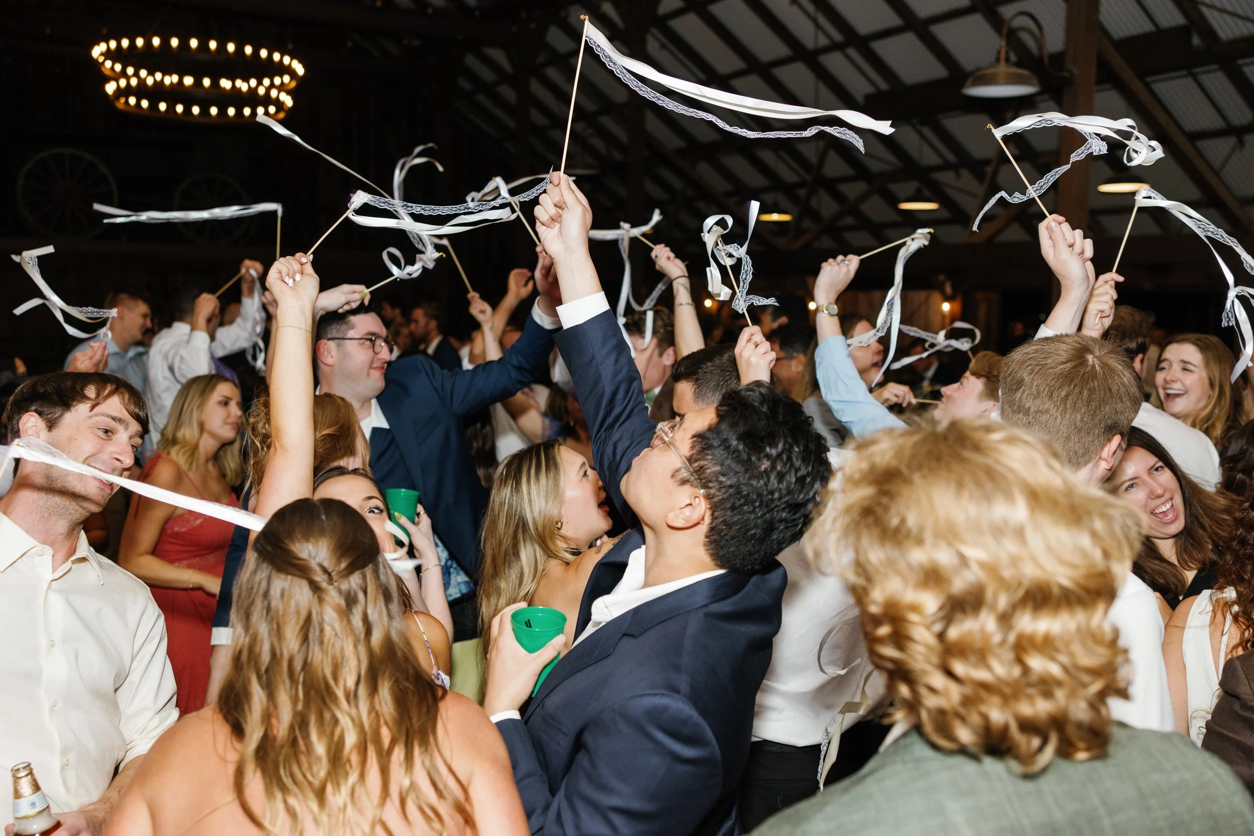 Photo Credit: Kaitie Brainerd, The White Barn, San Luis Obispo Wedding (At the end of the wedding dance party, a couple's friends and family are all on the dance floor, drinks in one hand, with a small white streamer in the other. They're all waving 
