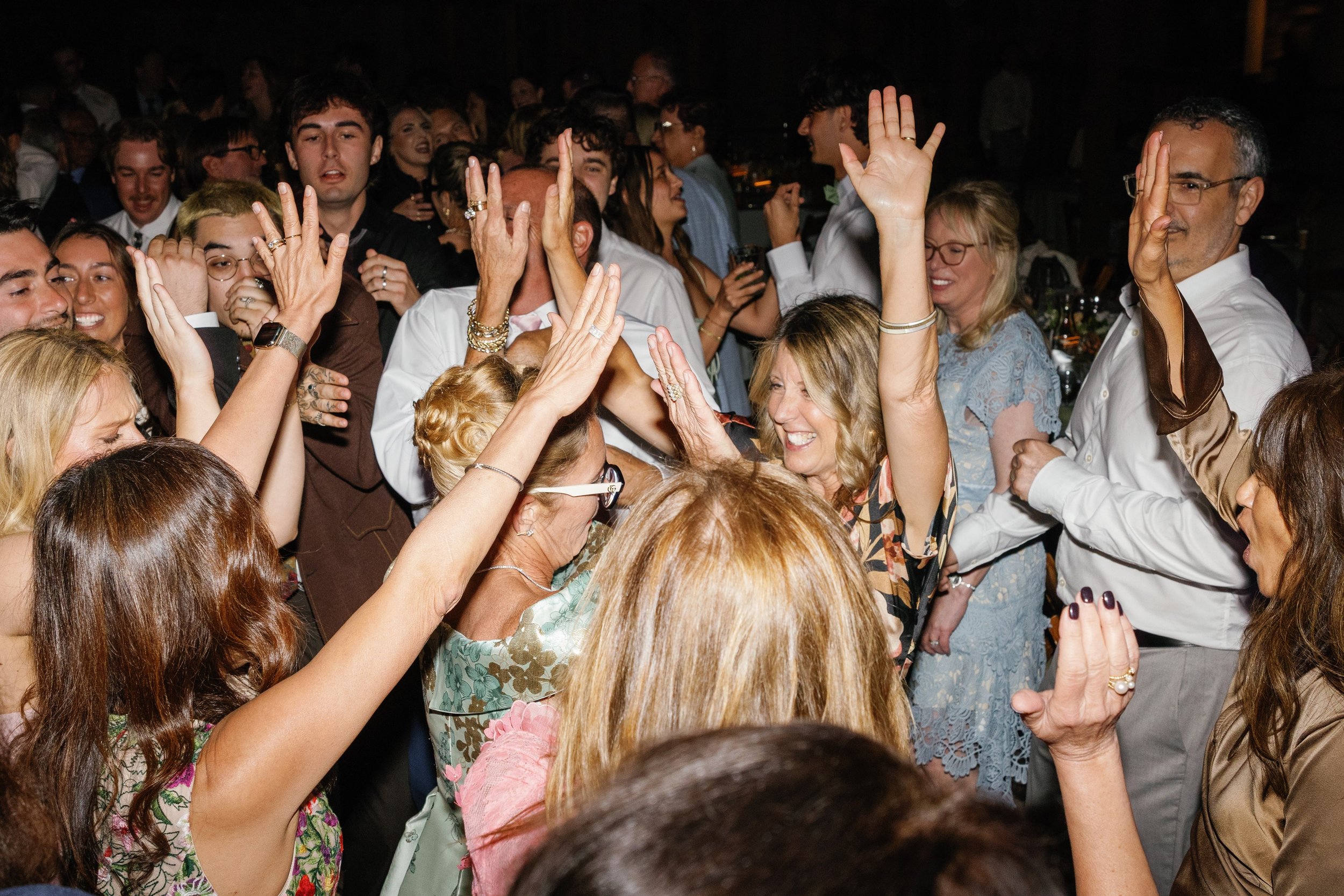 Photo Credit: Kaitie Brainerd, The White Barn, San Luis Obispo Wedding (A couple's friends and family are all on the dance floor. Several of their family have their hands in the air and many smiling faces can be seen.)