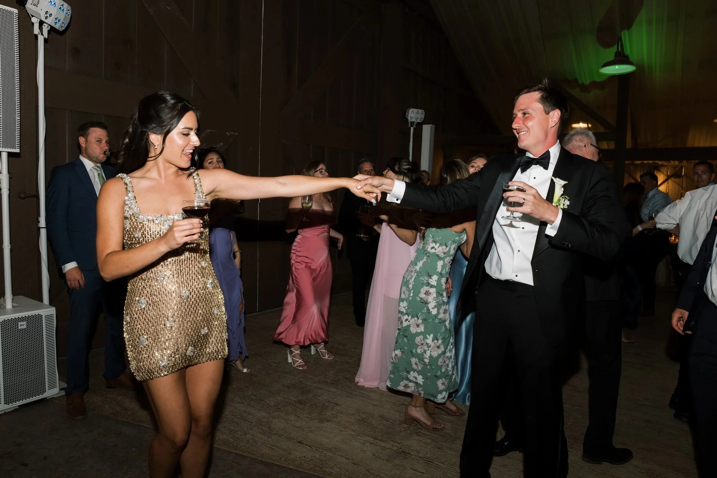 Photo Credit: Ellie Koleen Photography, The White Barn, San Luis Obispo Wedding (A bride and groom dance together on their wedding night. They're arms length apart, holding hands, smiling at each other, and holding a drink in the other hand. Behind t