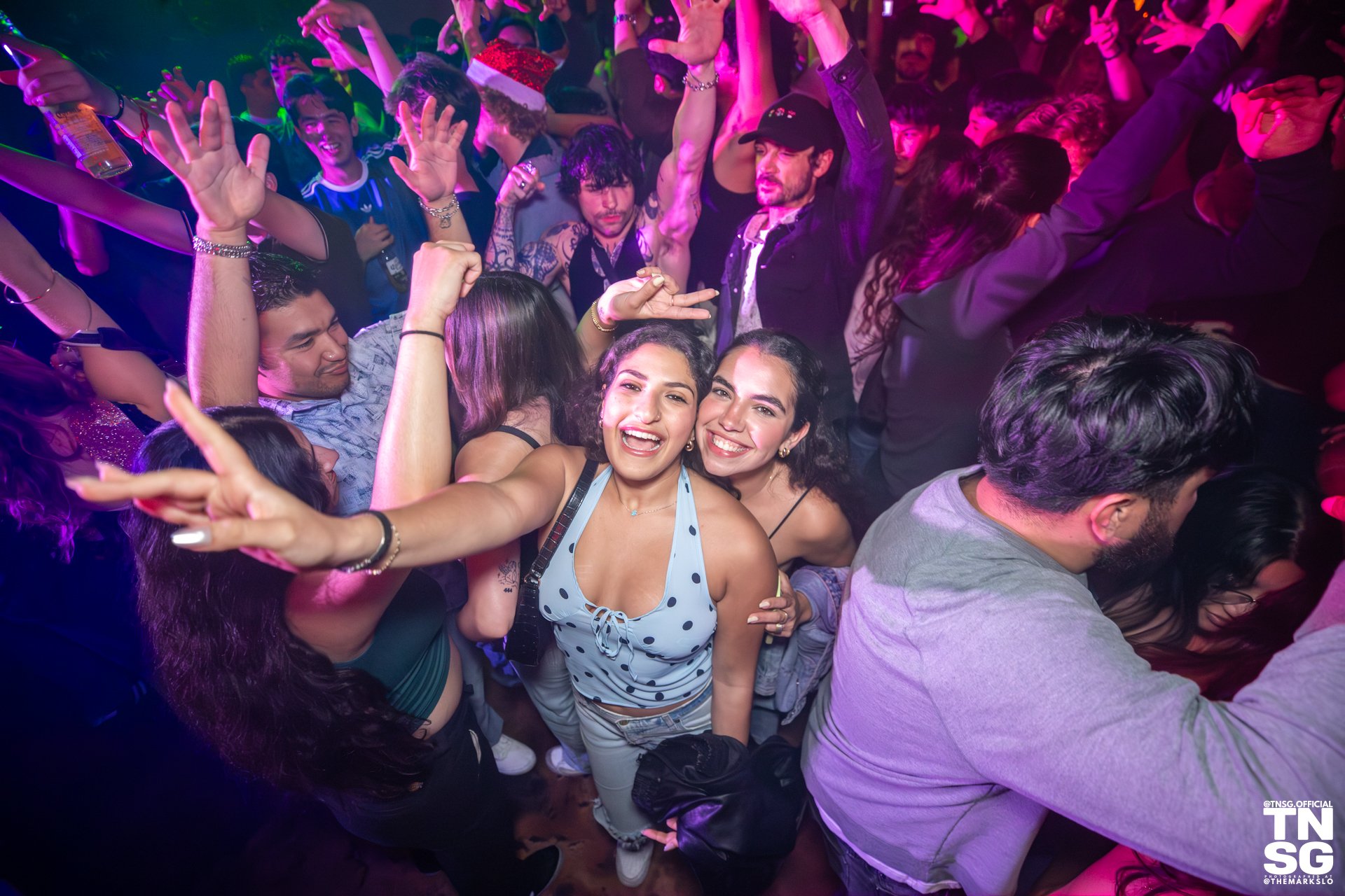A packed dance floor at The Mark in downtown San Luis Obispo. Everyone has their hands in the air and this photo focuses on two smiling young women as they look into the camera!