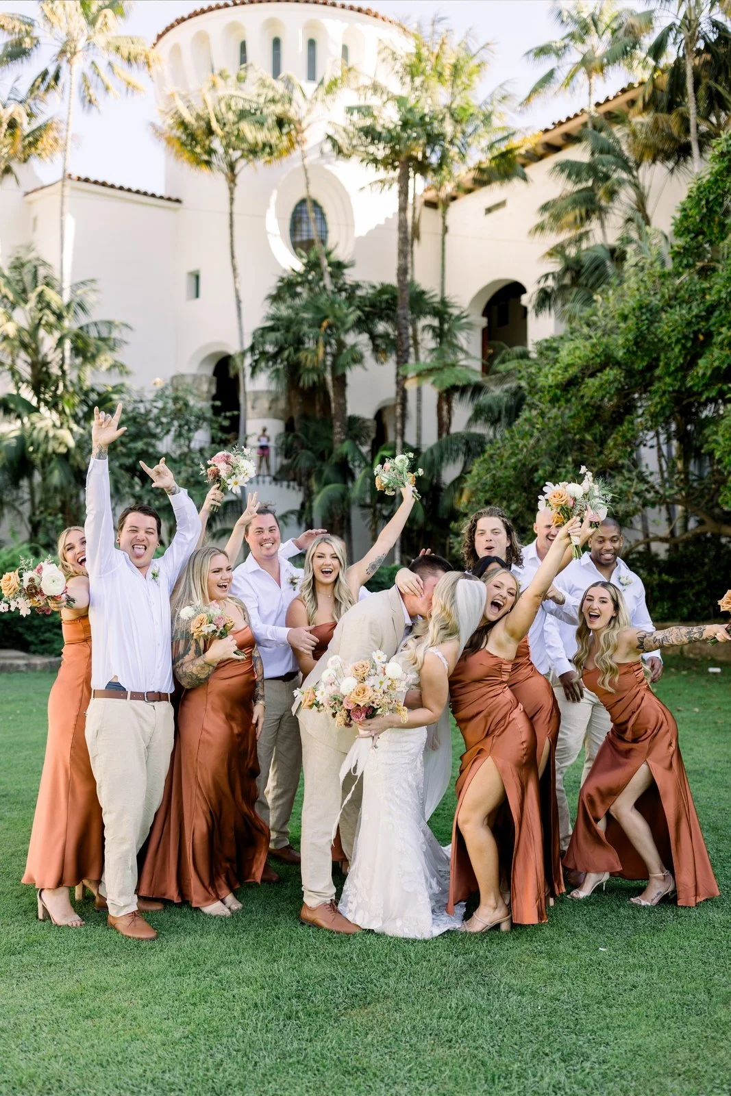A couple and their wedding party stand in the Sunken Gardens at the Santa Barbara Courthouse. The bride and groom are kissing while the friends cheer in celebration!