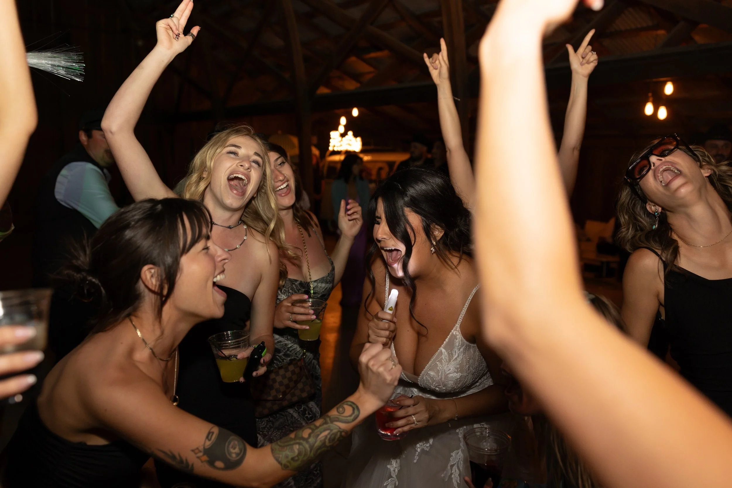 Photo Credit: J Leigh Photography, Tar Creek Ranch, Arroyo Grande Wedding (A bride dances on her weeding night. She's singing into an LED wand like it's a microphone. Many of her girlfriends are dancing with her, have their hands in the air, and sing