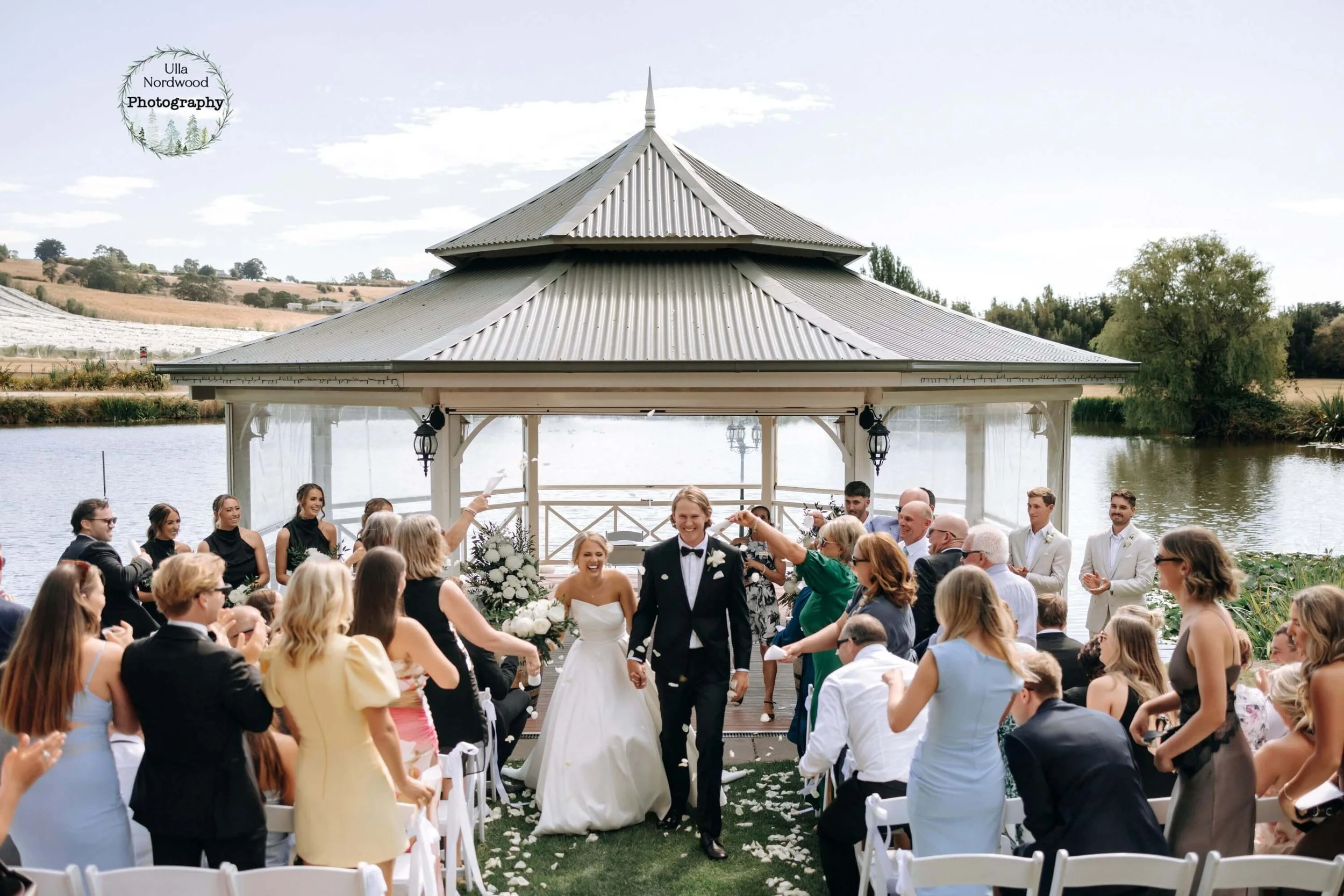 Bride and groom walking through guests and confetti at their lakeside pavilion wedding ceremony, Josef Chromy Wines, Tasmania