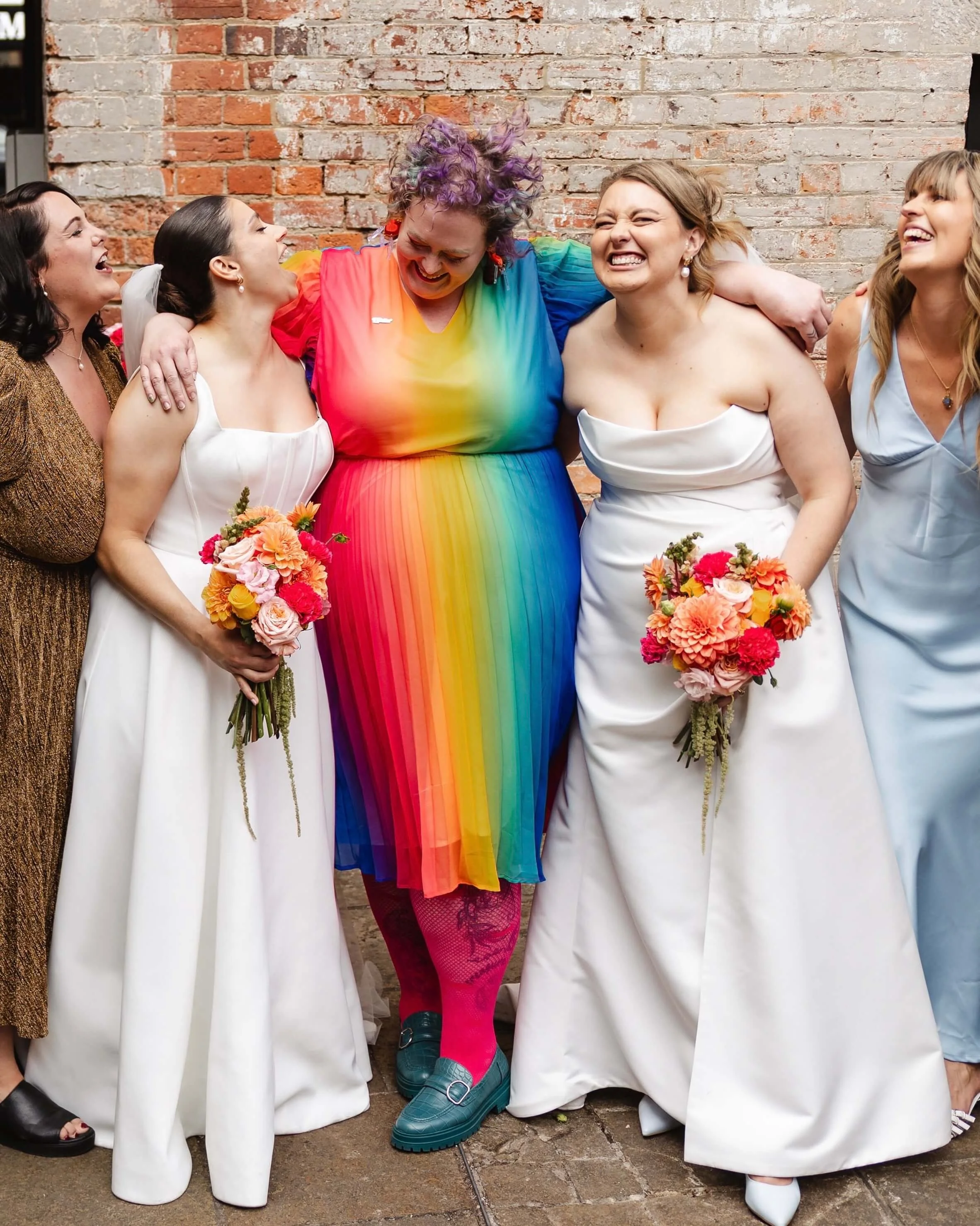 celebrant in rainbow dress standing between two parties in wedding dresses holding bouquets