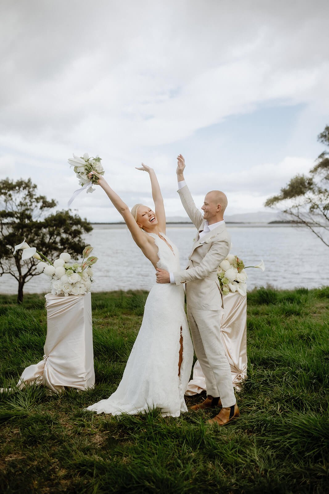 Bride and groom celebrating with raised arms after their waterfront elopement ceremony at Iron Bay Creek Estate