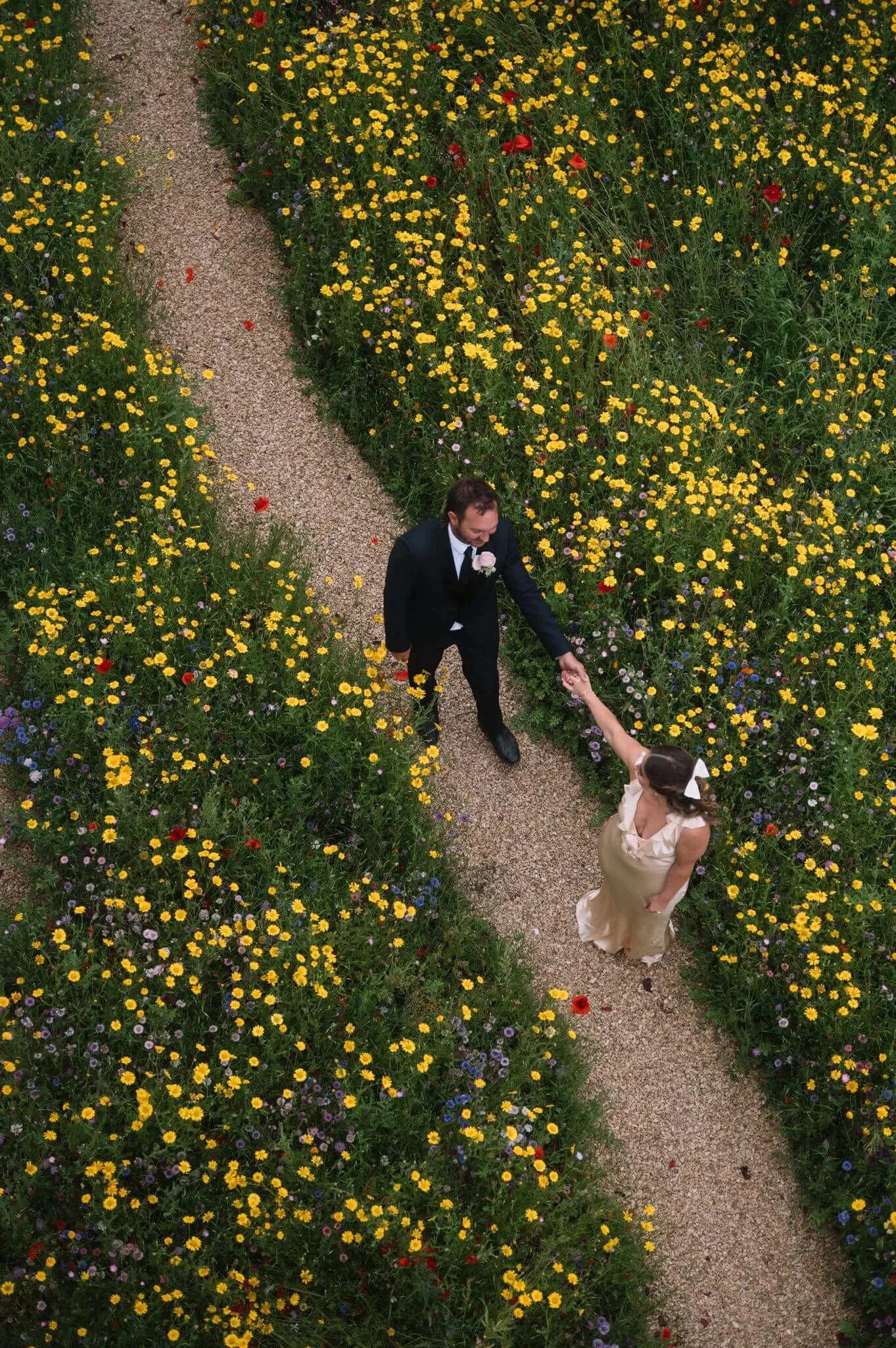 Aerial view of a couple holding hands along a gravel path through wildflowers at Palazzo Campania, elopement setting
