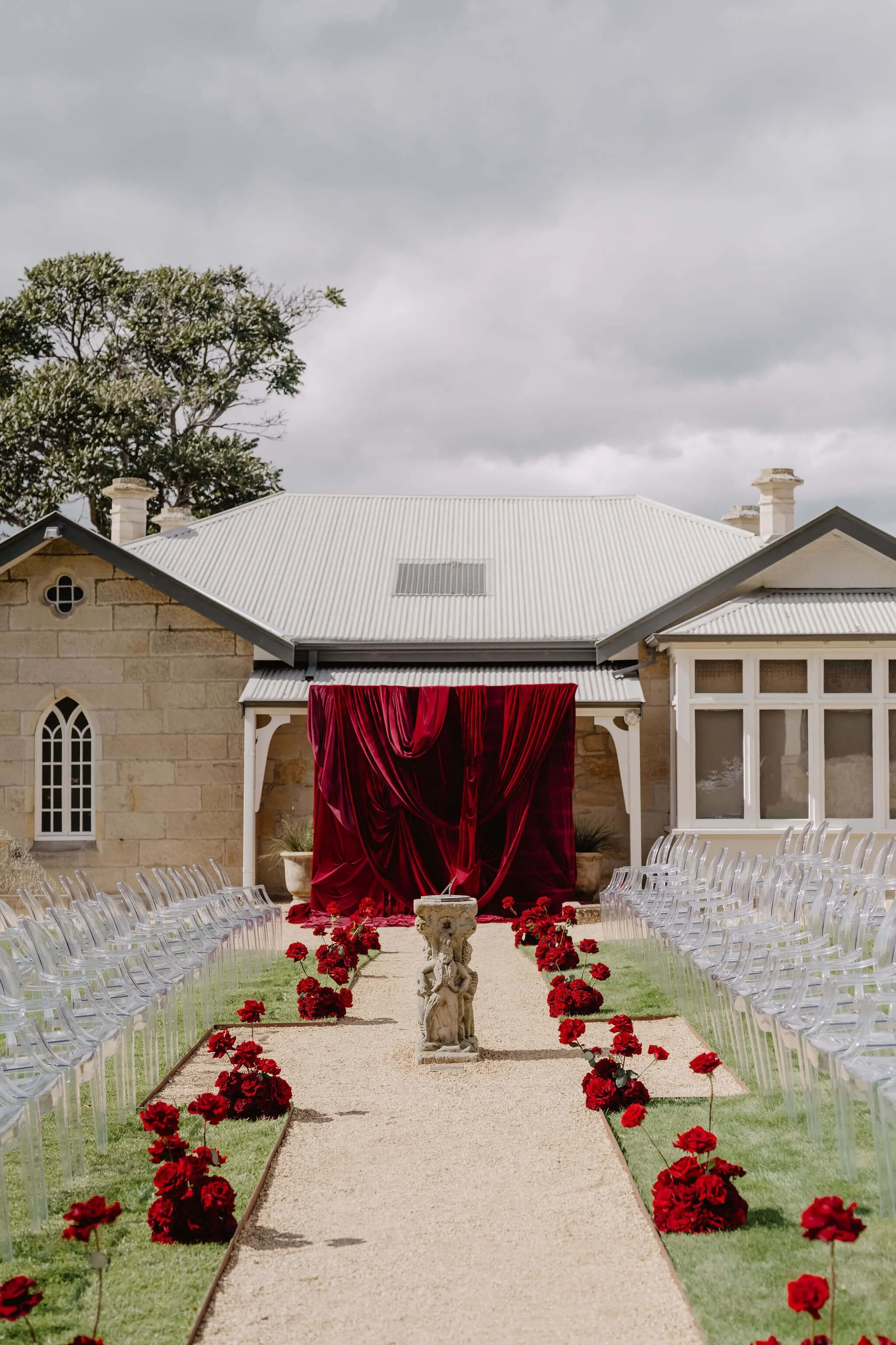 ceremony setup with catwalk style seating and red roses lining aisle and red velvet backdrop hung against building