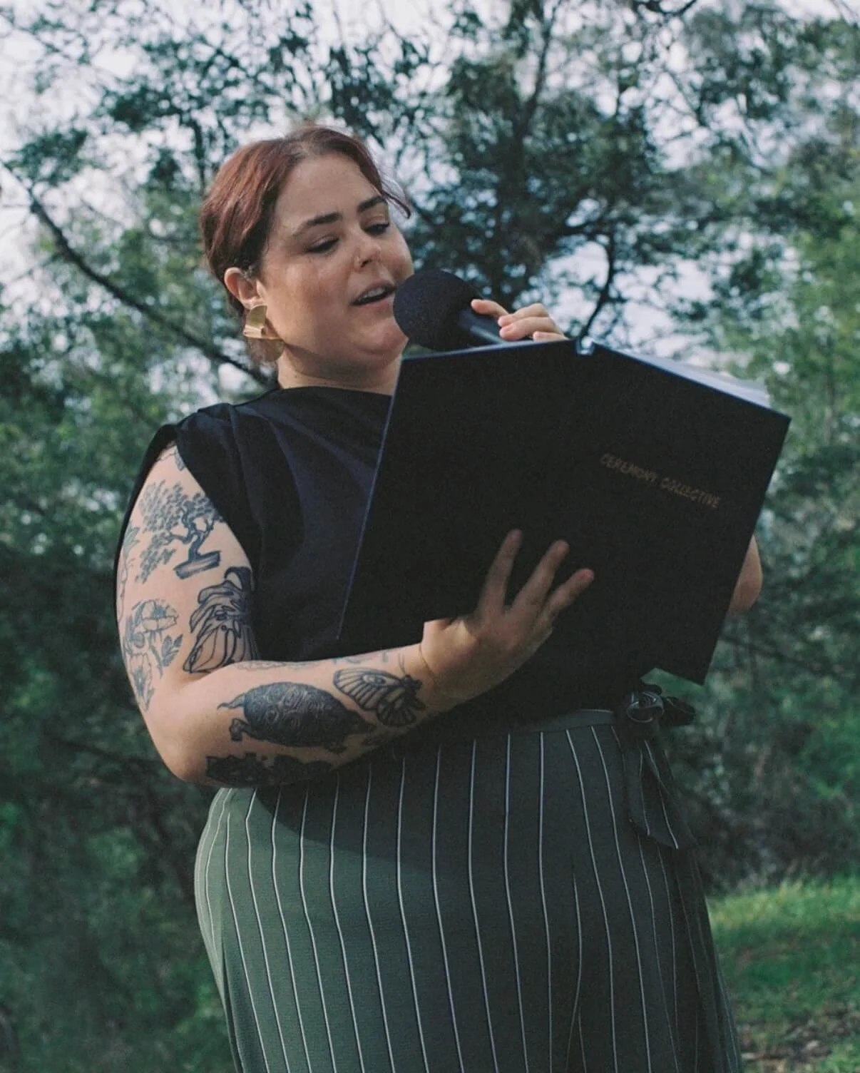 Ceremony Collective celebrant reading from a ceremony folder into a microphone during an outdoor wedding ceremony
