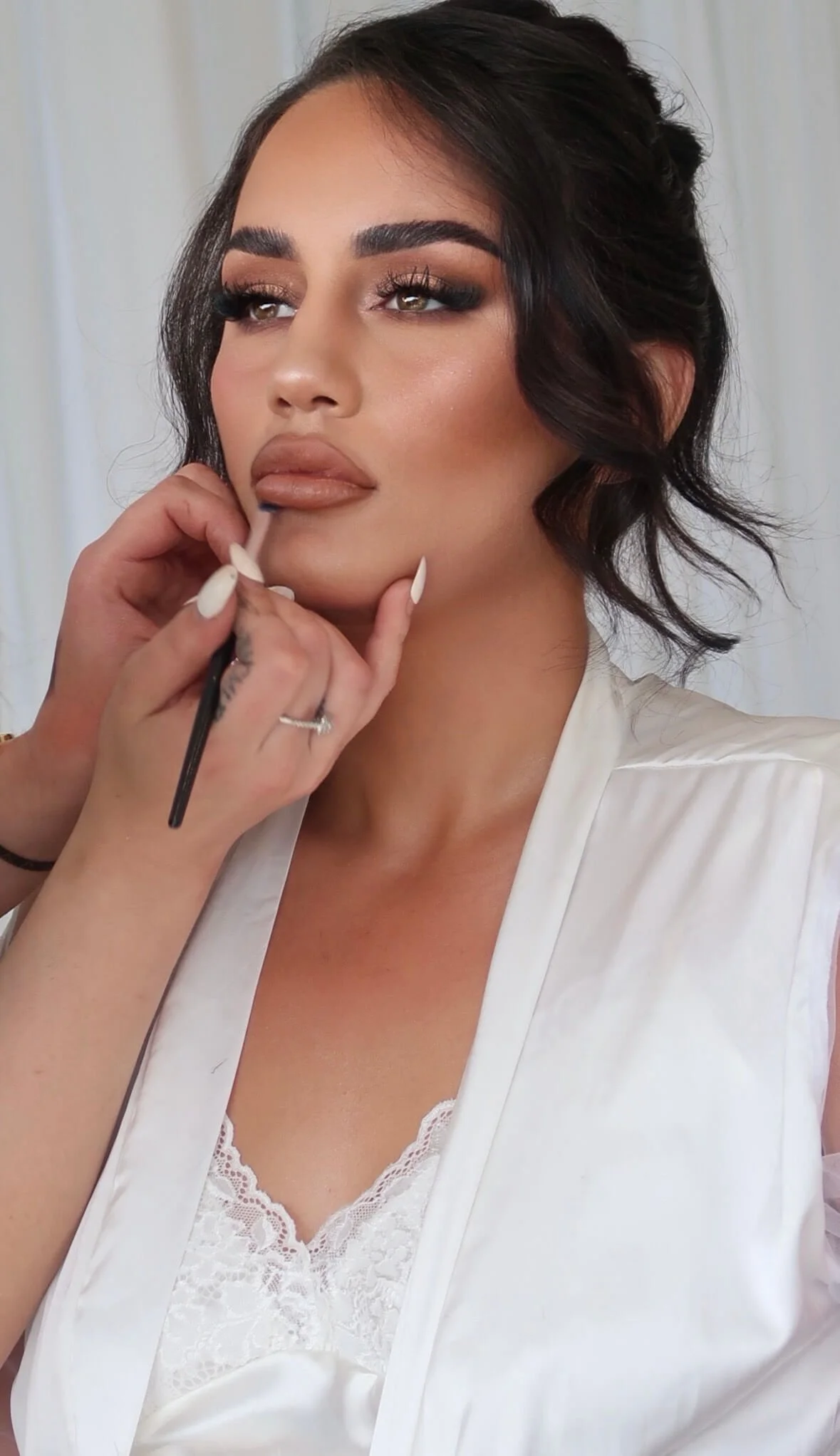 makeup artist holding lip liner brush against brides lips in white gown