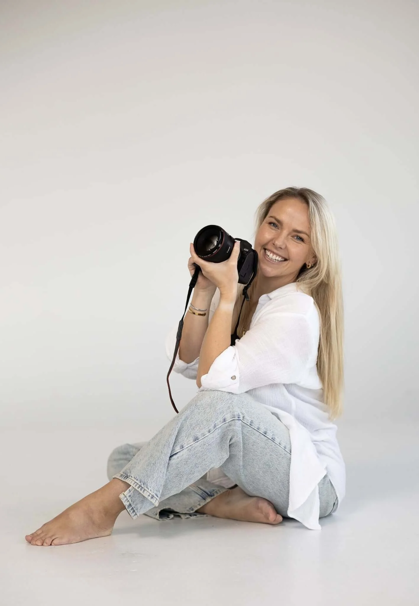 Lee Louise, Tasmanian wedding photographer, sitting on the floor holding a camera and smiling