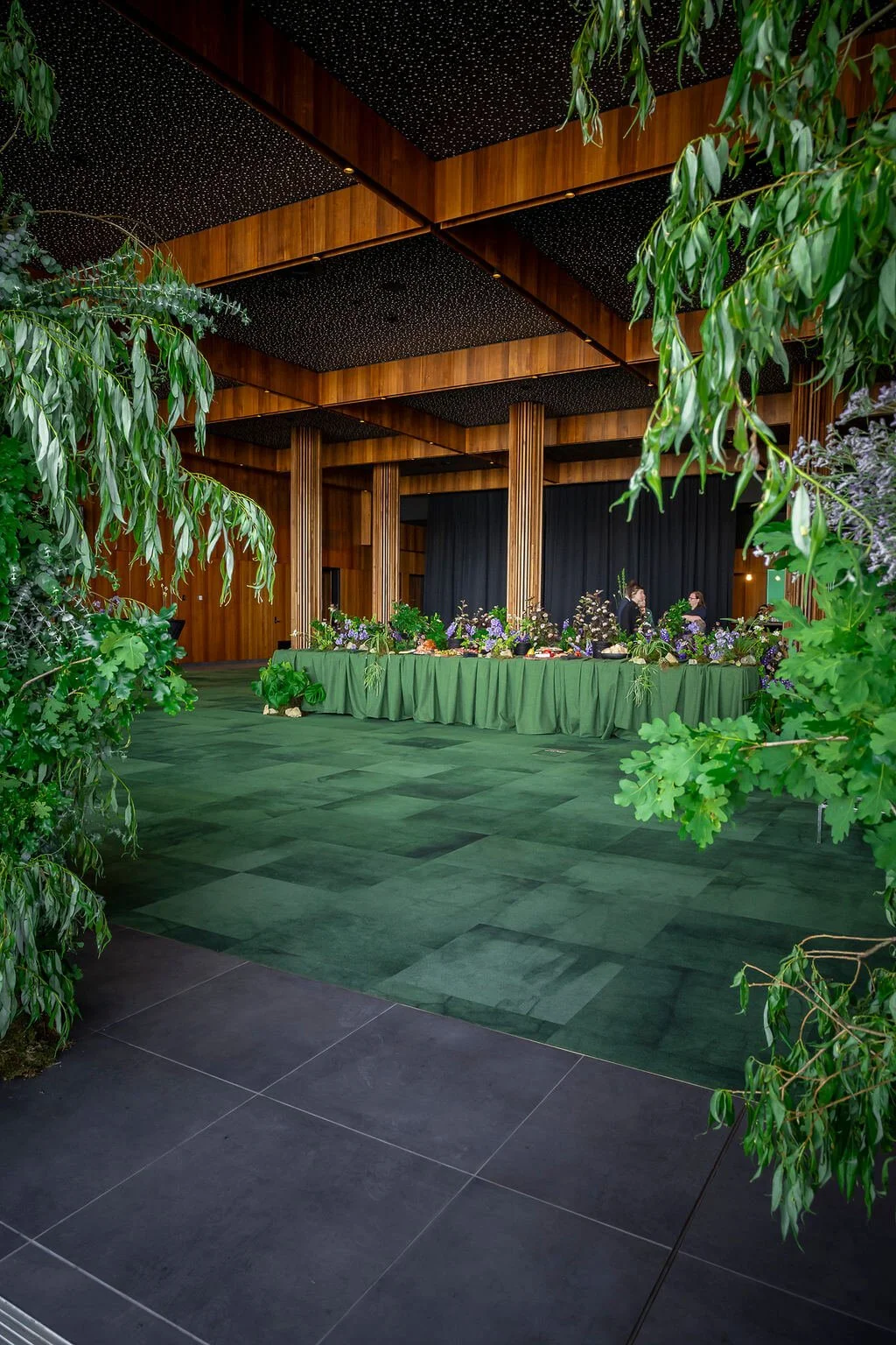 Long banquet table with green linen and native floral arrangements set up for a wedding reception under timber ceiling beams at MyState Bank Arena, Hobart