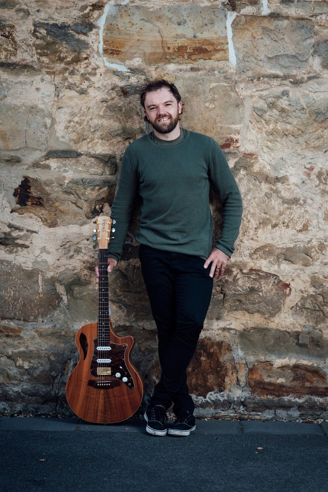 a man holding a guitar standing by a wall