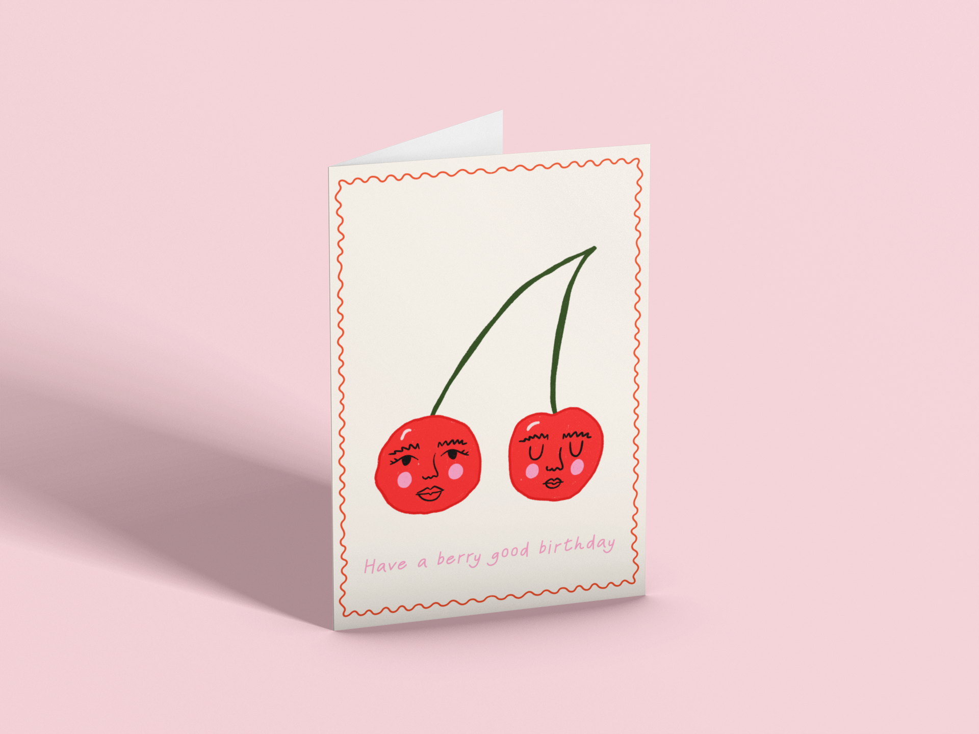 Birthday card with two cartoon cherries with faces, pink cheeks, and closed eyes, surrounded by a red-stitched border, on a pink background. Text reads, 'Have a berry good birthday'.