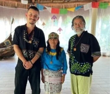 Three people smiling at a cultural event, with colorful flags hanging overhead.