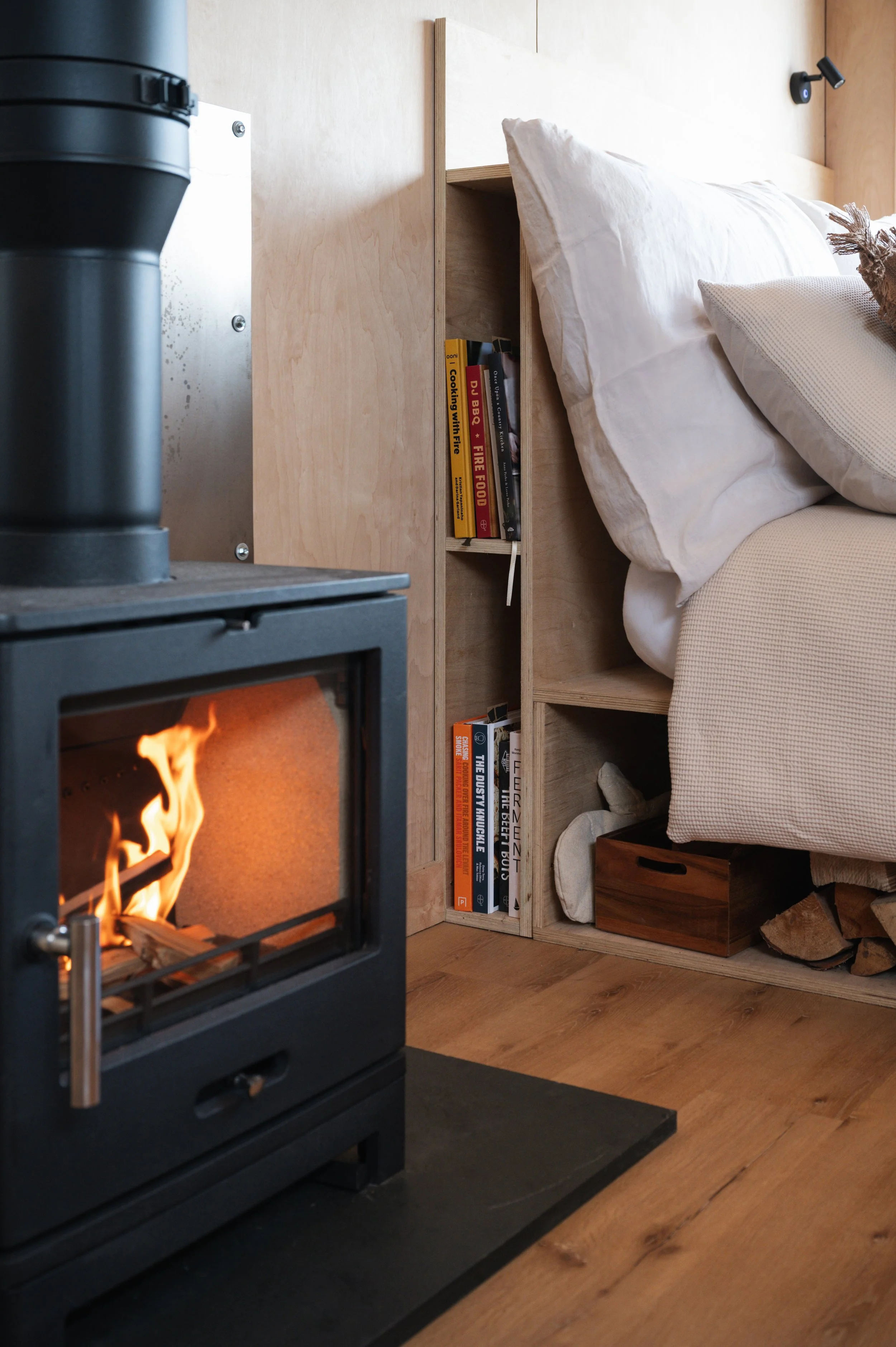 Warm and inviting tiny house interior with a wood-burning stove, soft bedding, and a built-in bookshelf — perfect for a relaxing countryside escape.